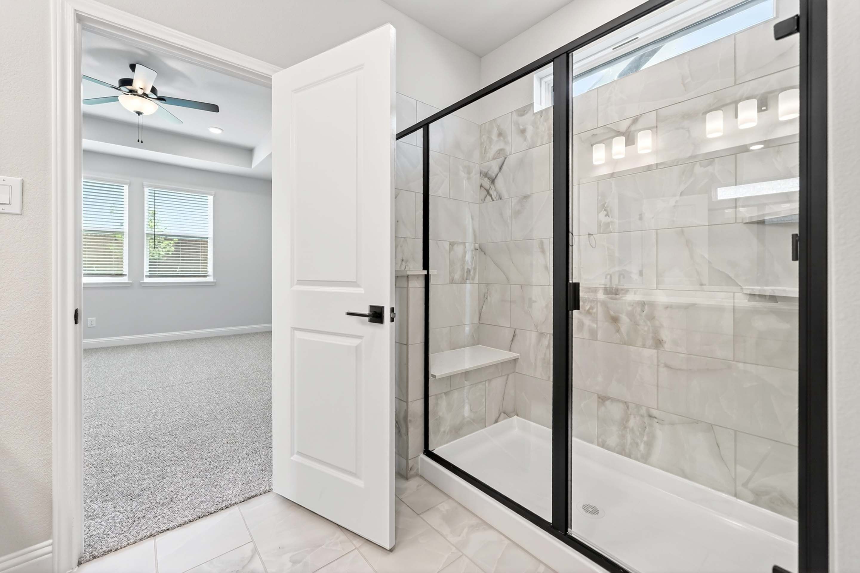 Master suite bath in The Holly N featuring a glass-enclosed walk-in shower with marble-look tile and black hardware.