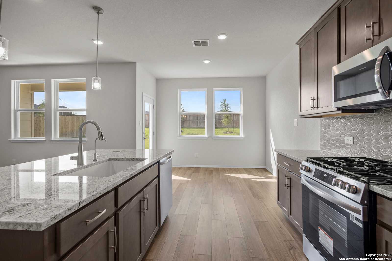 Open-concept kitchen with quartz island, stainless appliances, and backyard view in Davidson Homes The Asheville J, San Antonio