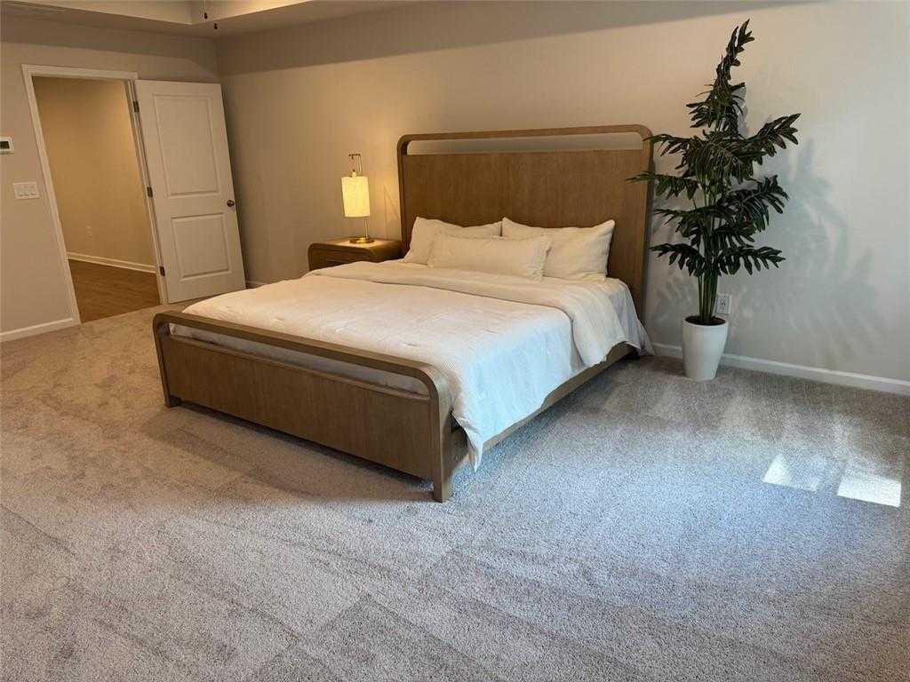 Spacious master bedroom with king bed, wooden headboard, bedside lamp, and potted tree in Davidson Homes The Cary A, Kennesaw, Georgia