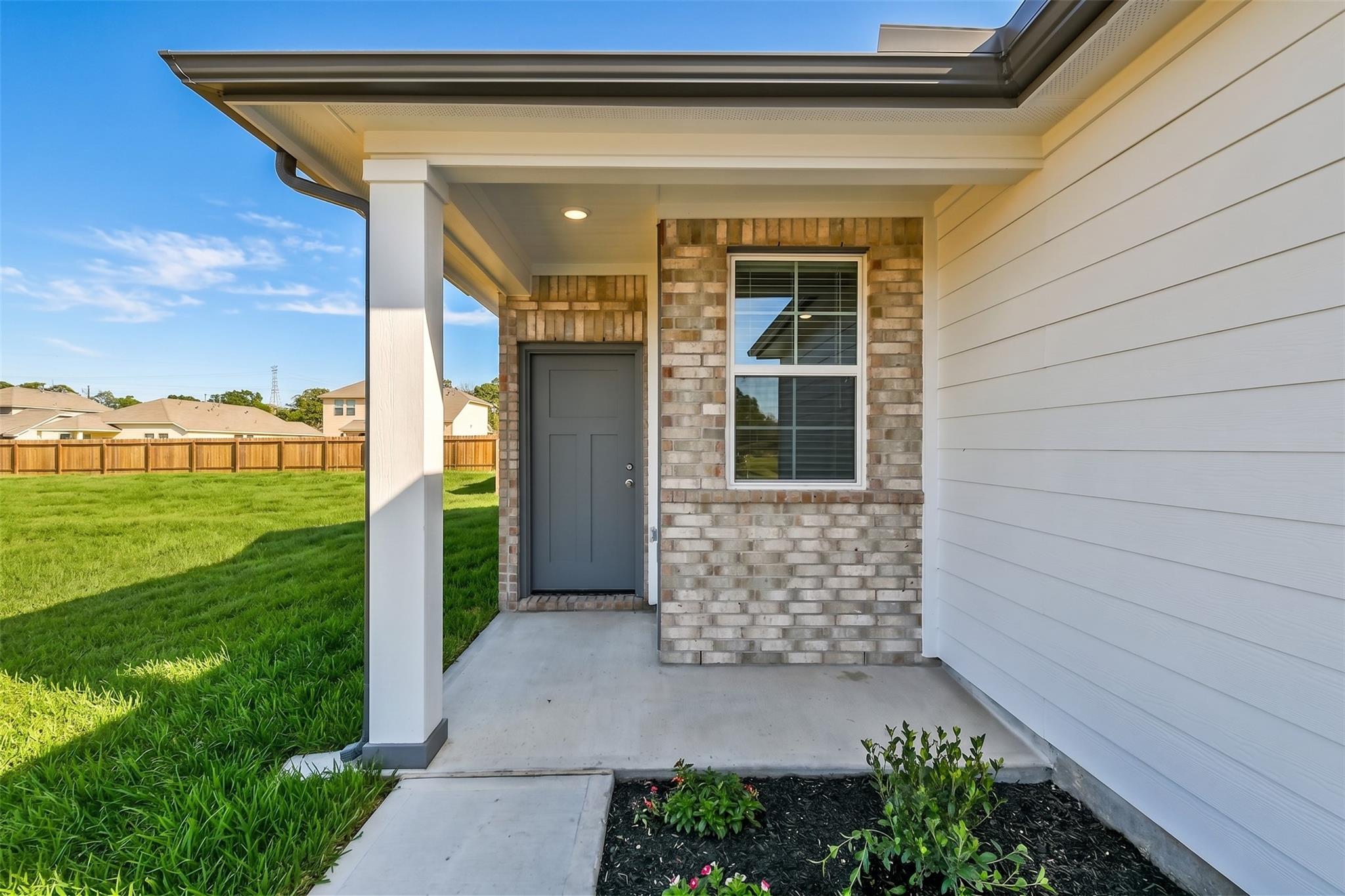 Covered entryway with brick facade and gray door of The Colorado F floor plan at Liberty Estates in Cleveland, Texas.