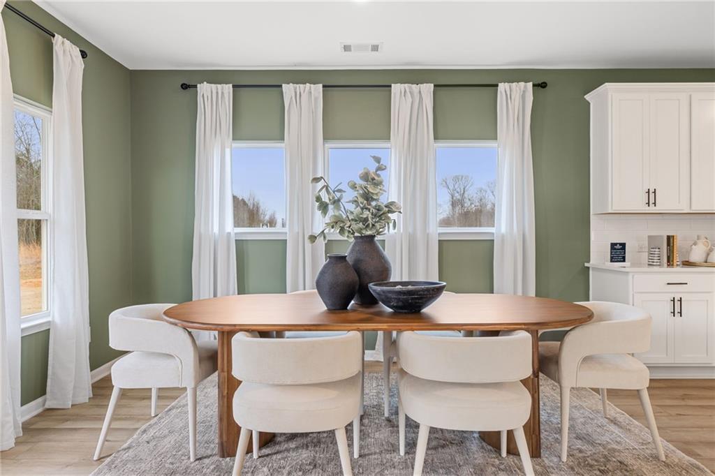 Elegant dining room featuring oval wooden table, white curved chairs, eucalyptus vases, sage green walls in The Rabun B, Canton, GA