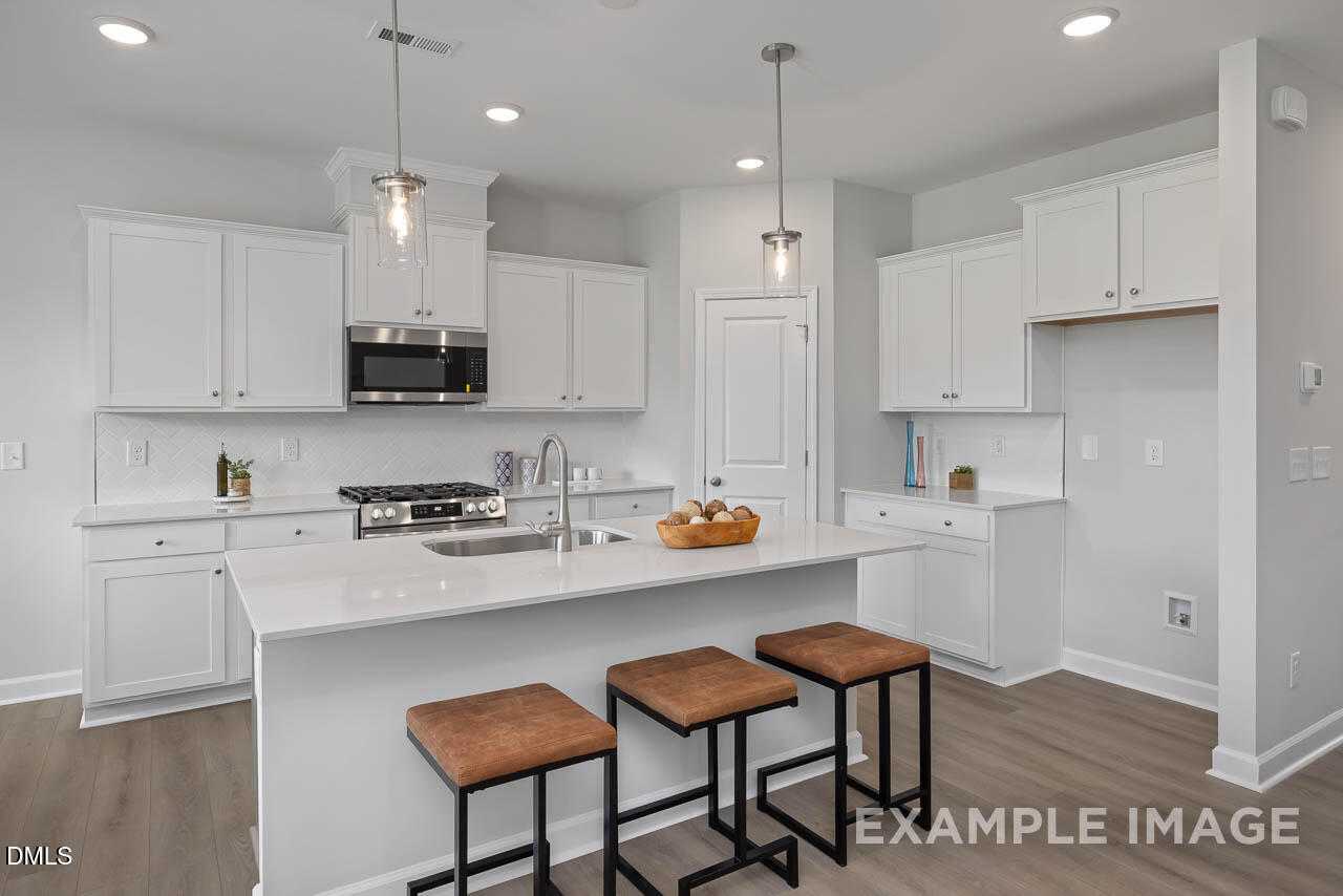 Modern white kitchen with quartz island, stainless appliances, and pendant lights in Davidson Homes The Warren, Fuquay-Varina, NC