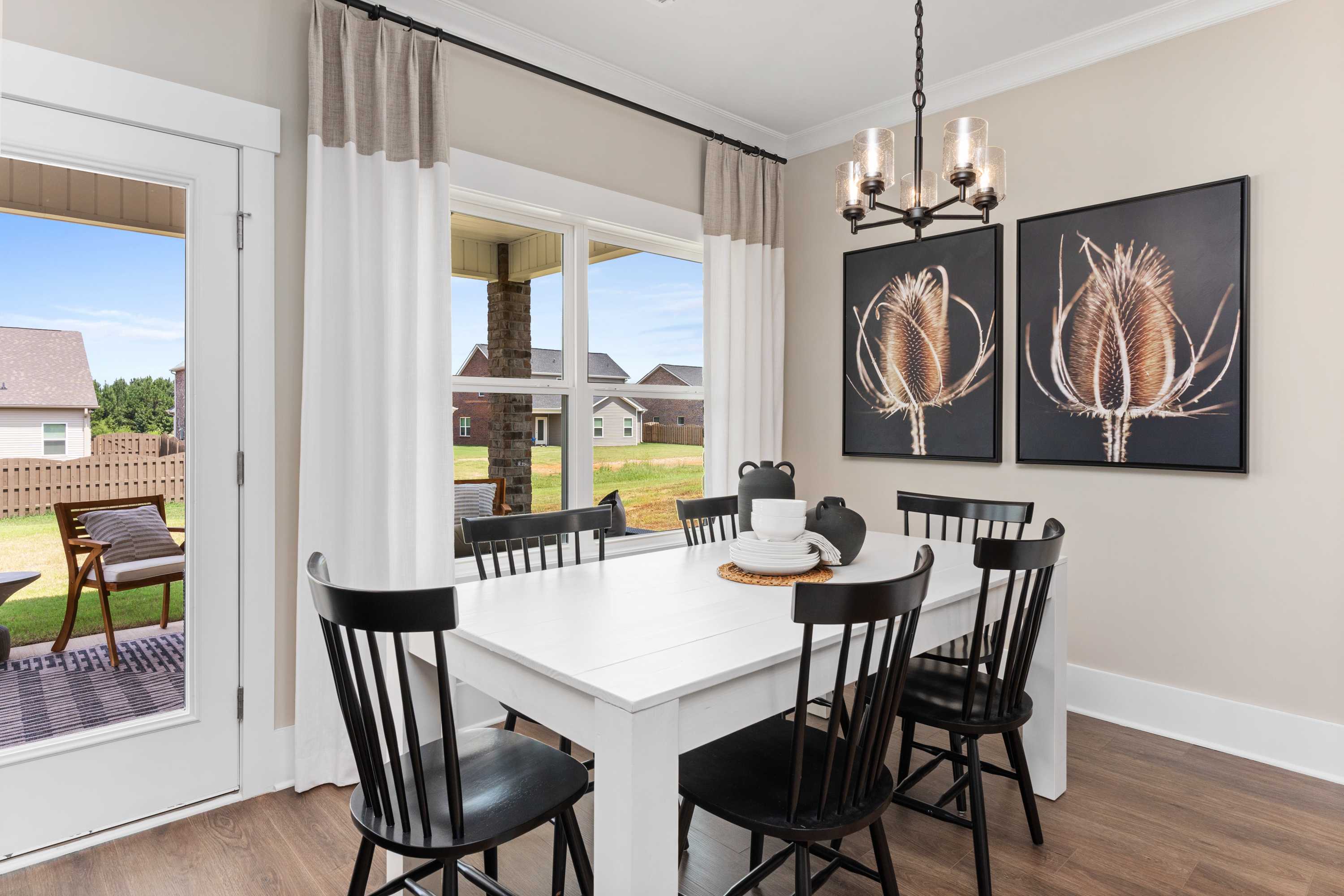 Bright dining room in The Shelby A featuring white rectangular table, black chairs, chandelier, botanical art, and patio view