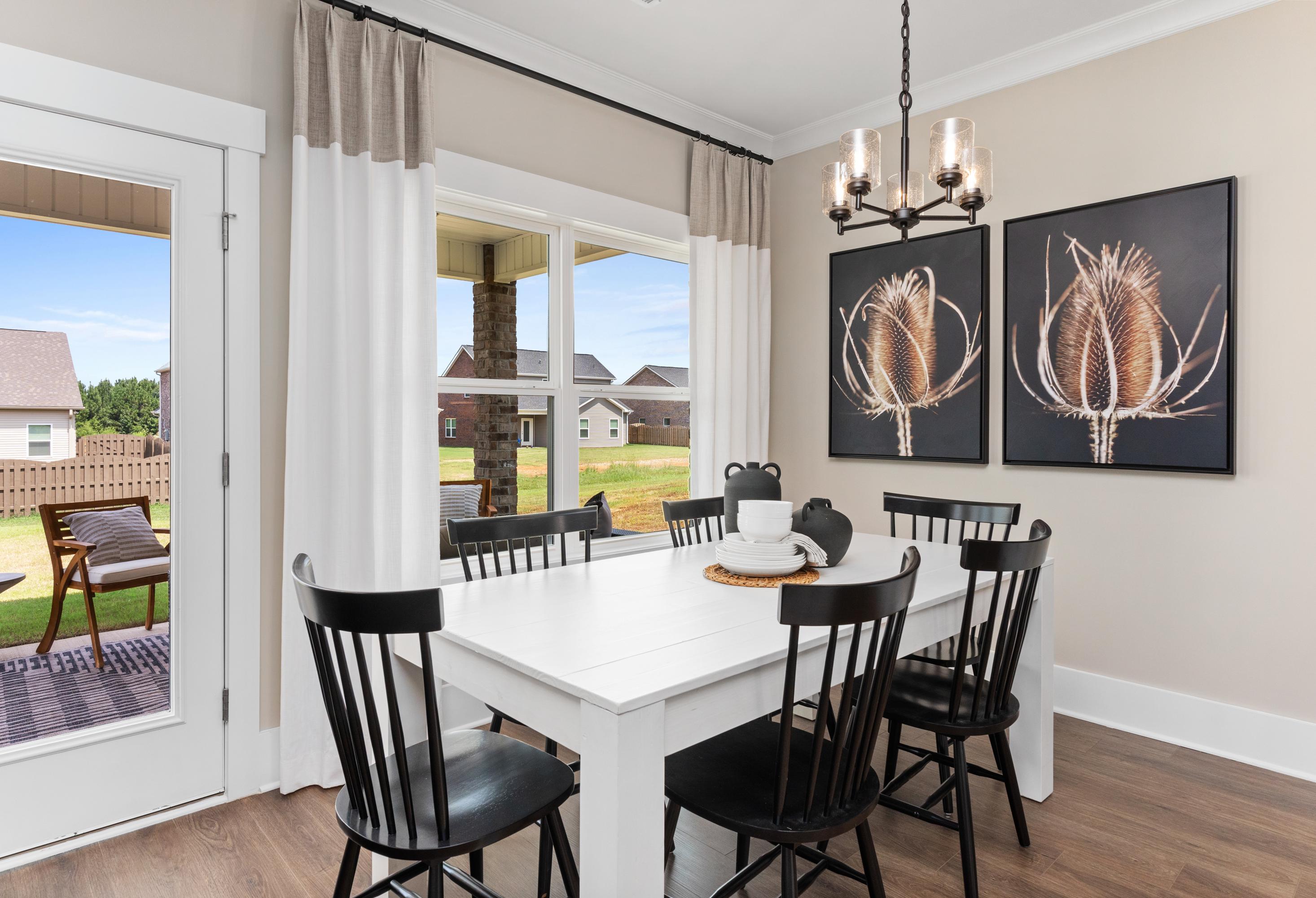 Spacious dining room in The Shelby B featuring white farmhouse table, black chairs, chandelier, and backyard view through French doors