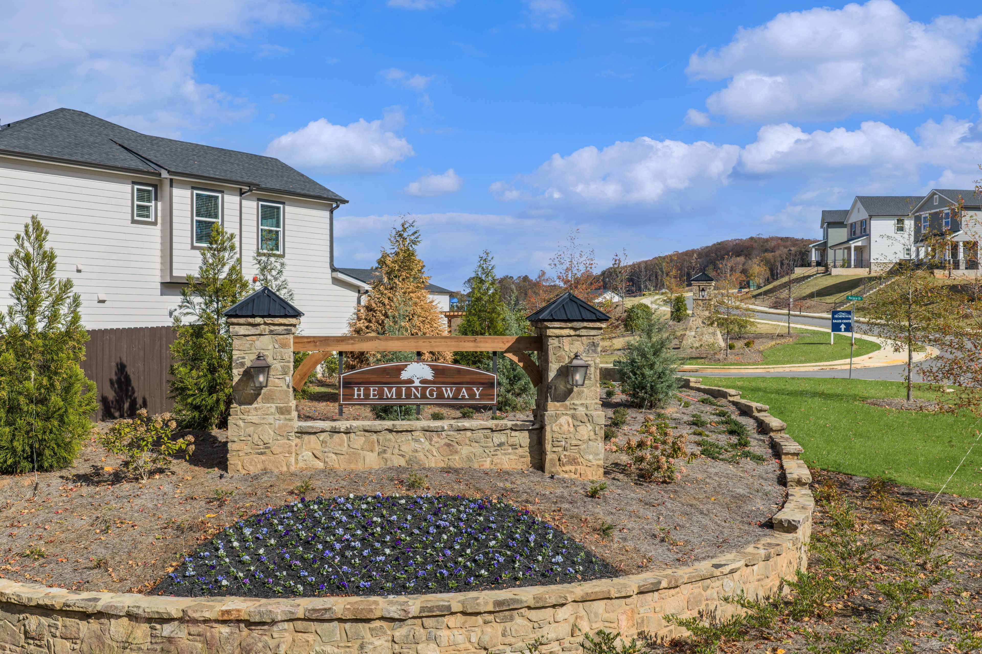 Hemingway neighborhood entrance in Cumming Georgia with stone pillars, landscaped shrubs, and modern homes