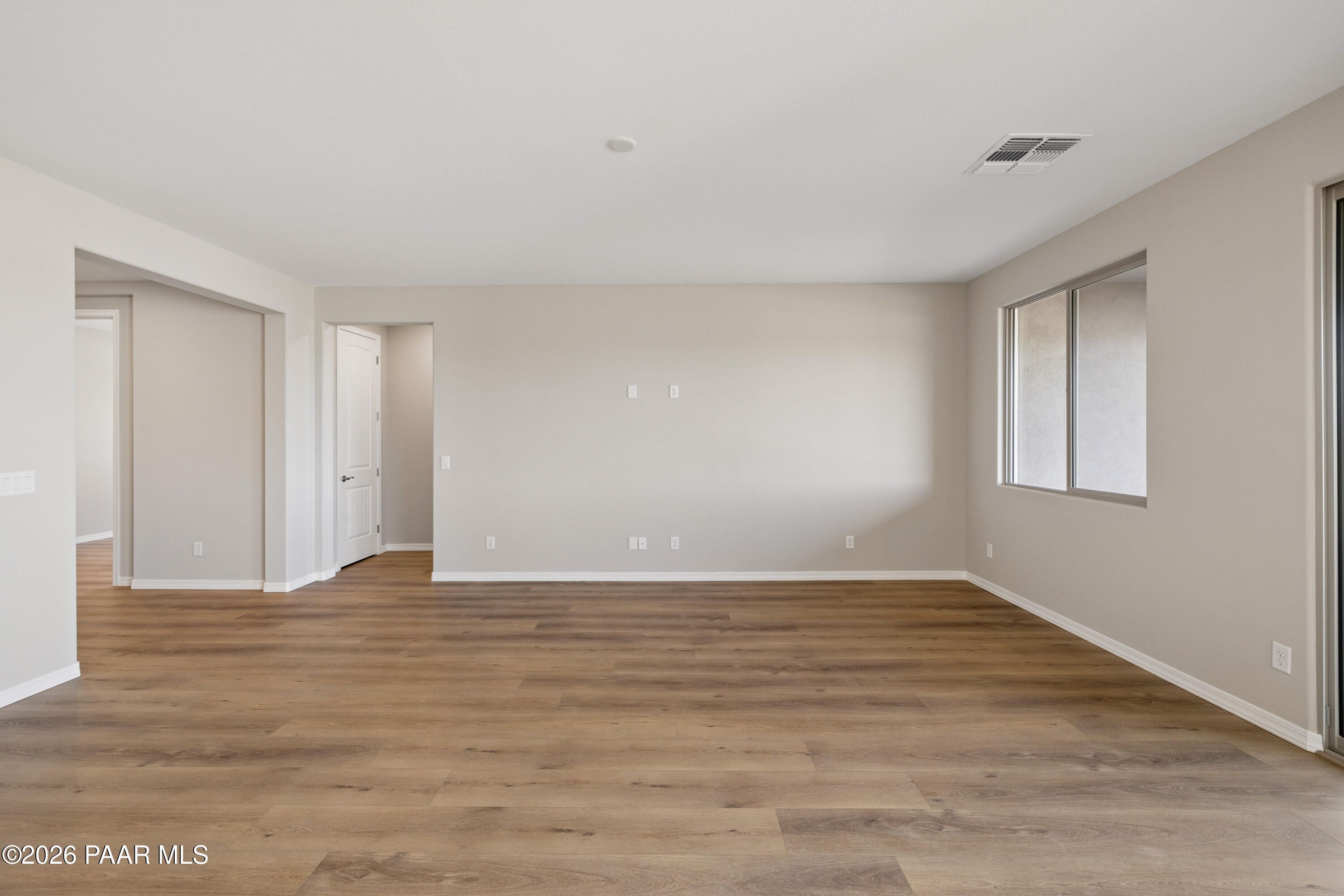 Spacious empty living room with beige walls, hardwood floors, and large windows in Davidson Homes The Harmony A, Prescott Valley, Arizona
