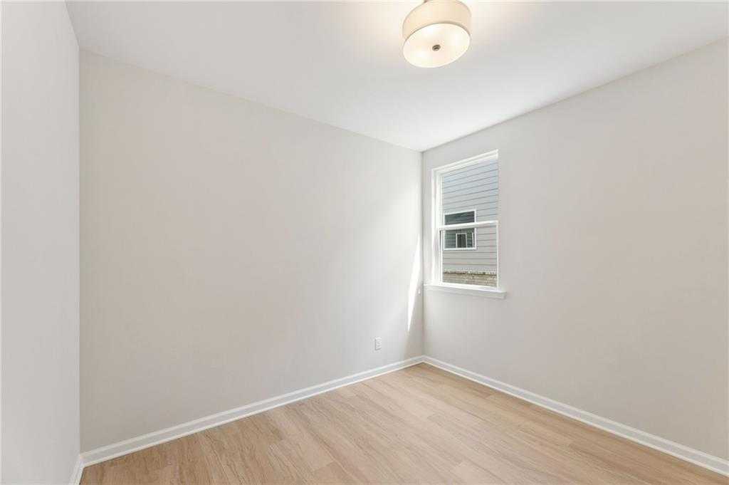 Bright empty secondary bedroom with neutral walls, hardwood floors, and window in Davidson Homes The Daphne C, Loganville, GA