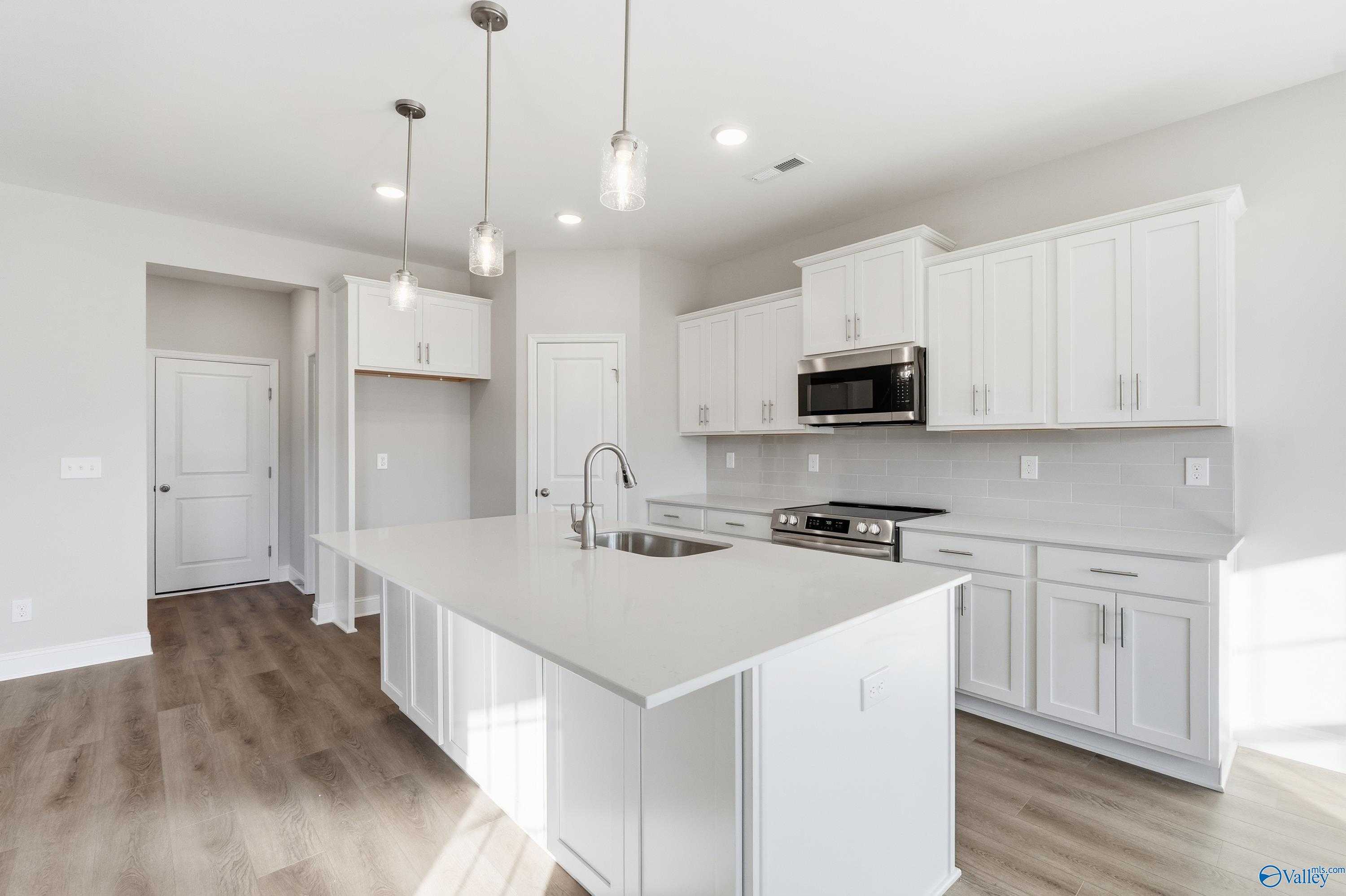 Modern white kitchen with quartz island, stainless appliances, pendant lights in The Montgomery B, Toney, Alabama