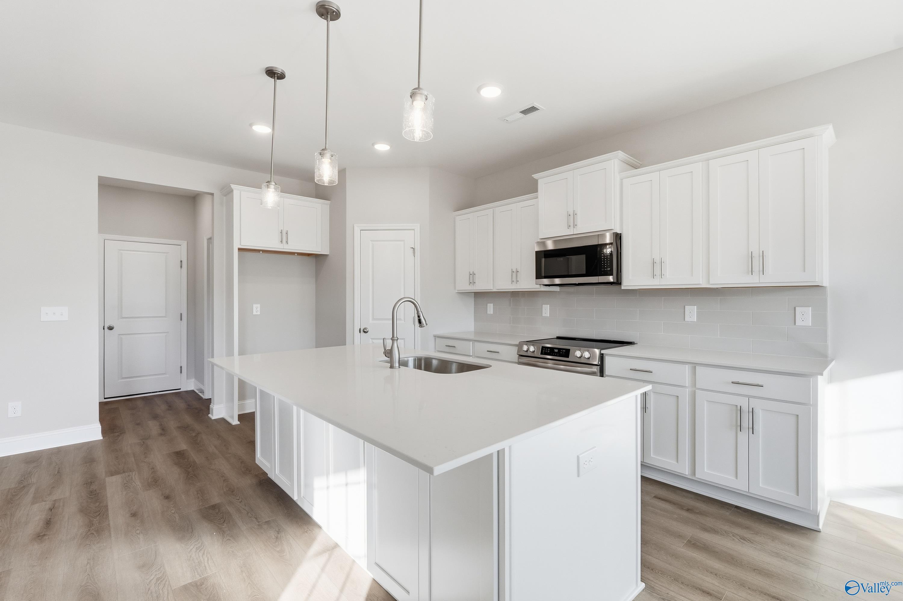 Modern white kitchen with large island, stainless appliances, and pendant lights in Davidson Homes The Montgomery B, Toney, Alabama