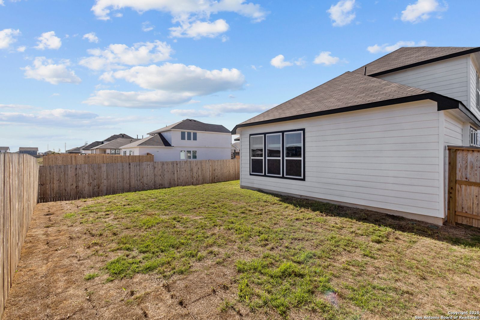 Side view of modern white single-story home with black trim, large windows, and fenced grassy backyard in Hannah Heights, Seguin, Texas