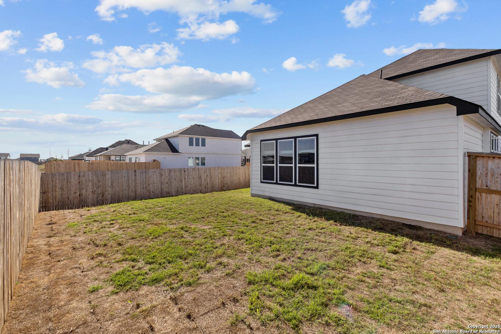 Side view of modern white single-story home with black trim, large windows, and fenced grassy backyard in Hannah Heights, Seguin, Texas