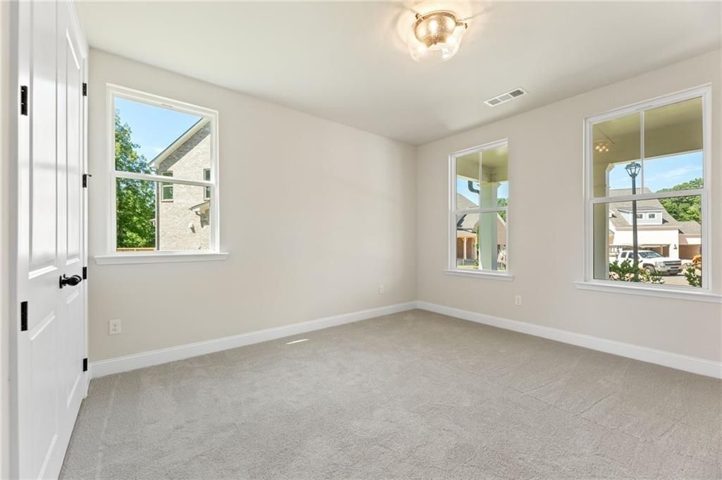 Bright bedroom with beige walls, carpet floor, chandelier light, and large windows overlooking landscape in Davidson Homes The Hickory E, Buford, GA