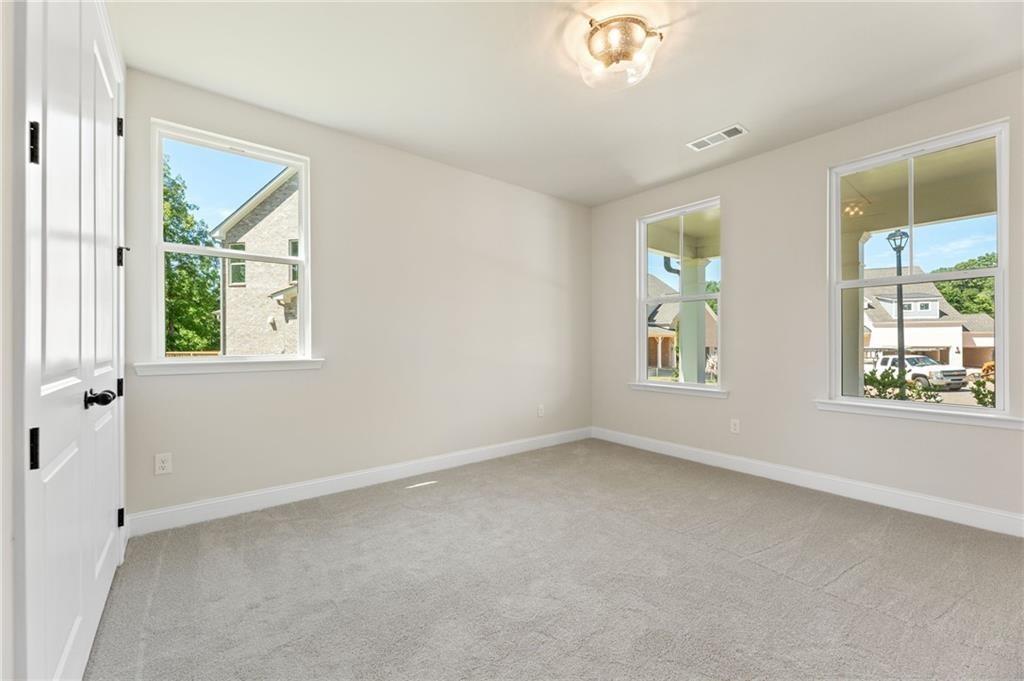 Bright bedroom with beige walls, carpet floor, chandelier light, and large windows overlooking landscape in Davidson Homes The Hickory E, Buford, GA