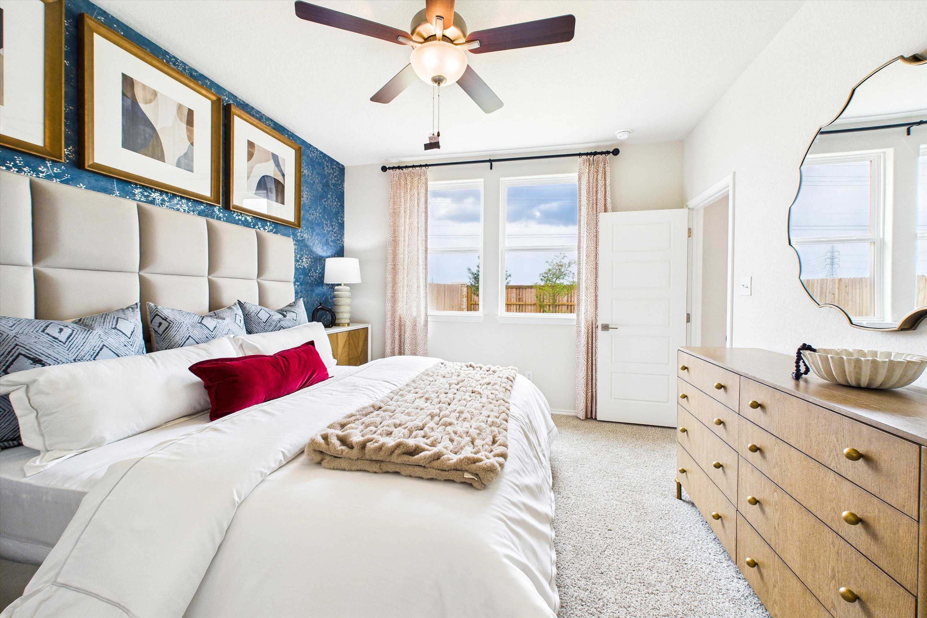 Modern primary bedroom in Agave San Antonio Texas with tufted beige headboard white bedding ceiling fan and abstract wall art