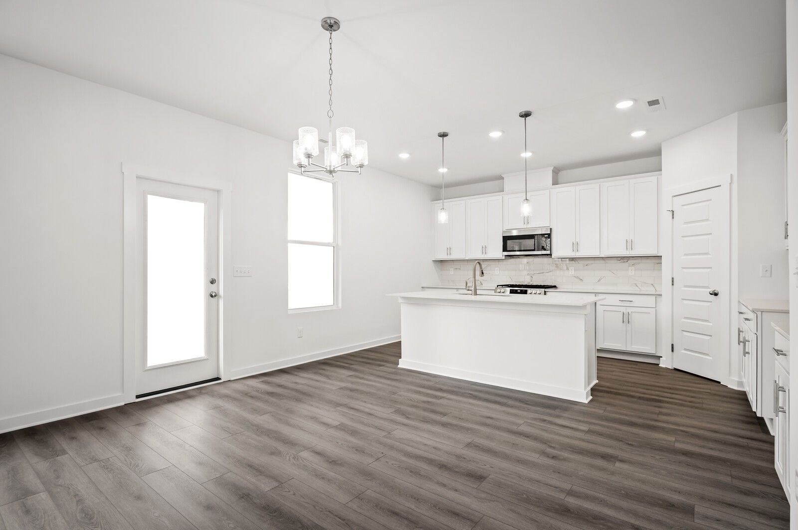 Modern white kitchen with island, pendant lighting, and wood-style flooring in The Logan C floor plan, Calista Farms.