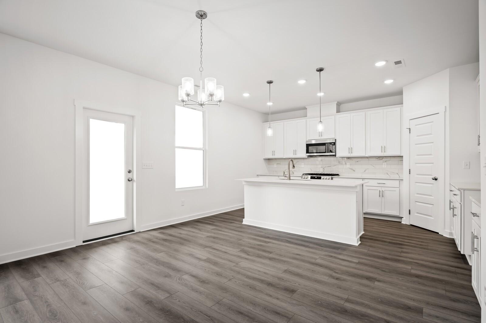 Modern white kitchen with island, pendant lighting, and wood-style flooring in The Logan C floor plan, Calista Farms.