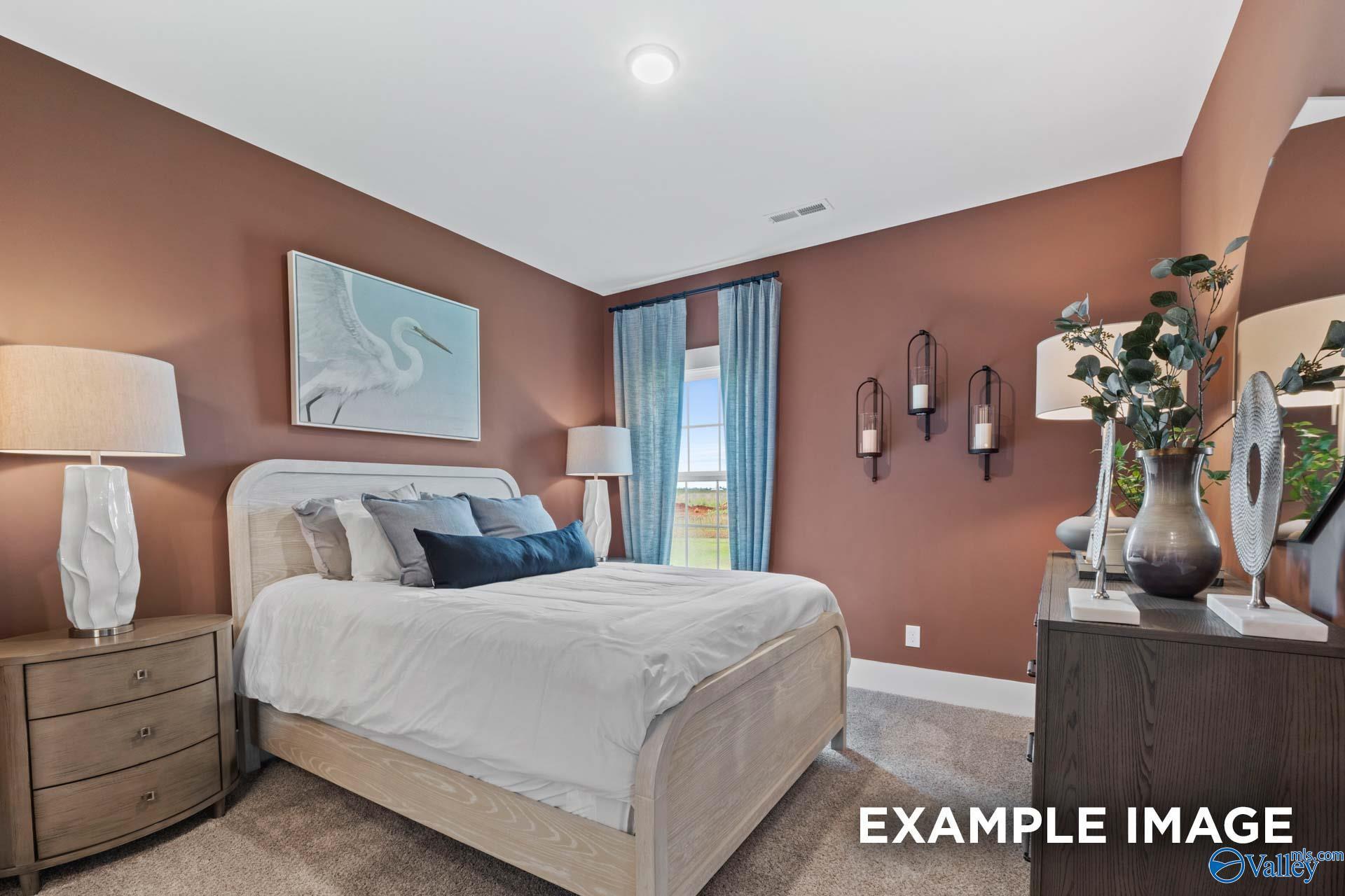 Cozy bedroom with beige walls, king bed in white linens, heron painting, blue curtains, and wooden furniture in Davidson Homes The Finleigh, Huntsville