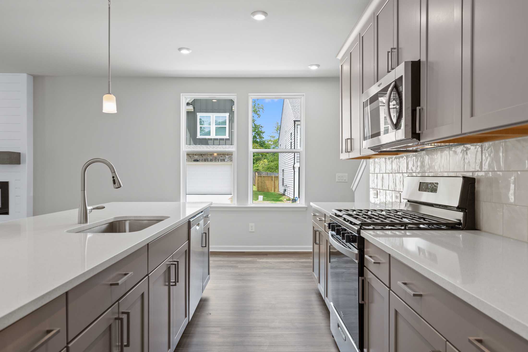 Spacious kitchen in The Cary A home with gray shaker cabinets, white quartz counters, stainless appliances, and backyard view