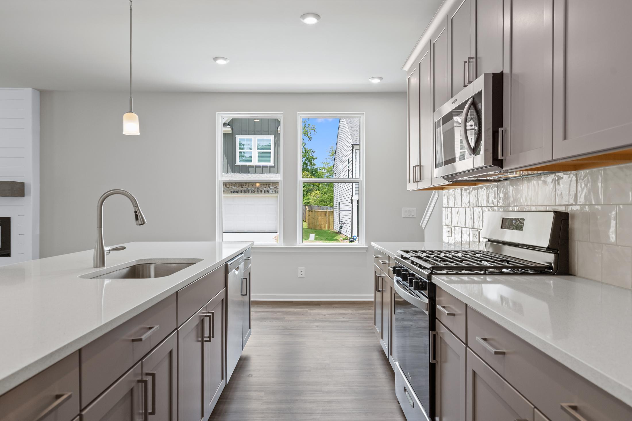 Spacious kitchen in The Cary A home with gray shaker cabinets, white quartz counters, stainless appliances, and backyard view