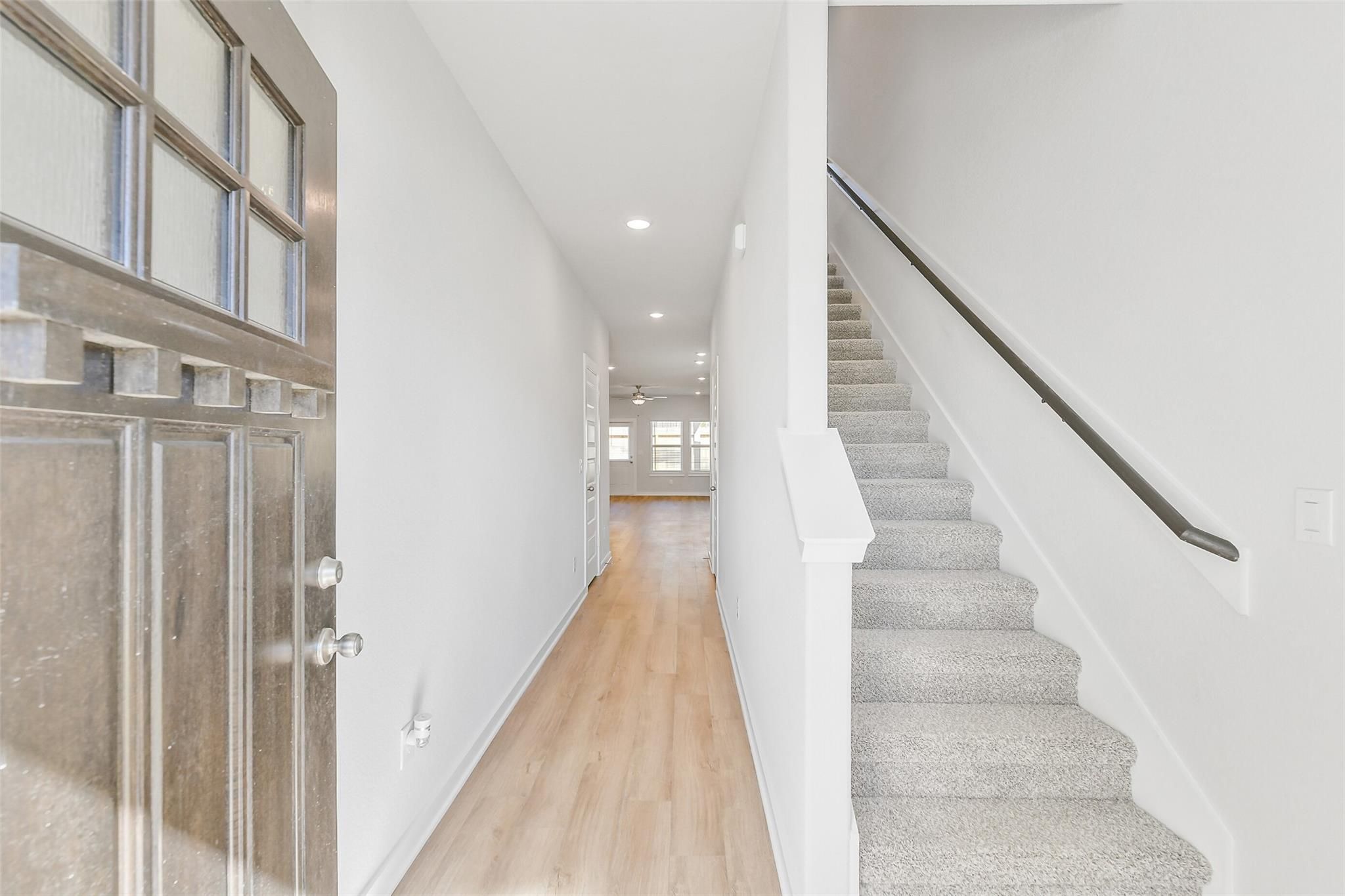 Bright entry foyer with glass-paneled front door, oak hardwood hallway, and carpeted staircase in Davidson Homes The Blanco E, Magnolia, Texas