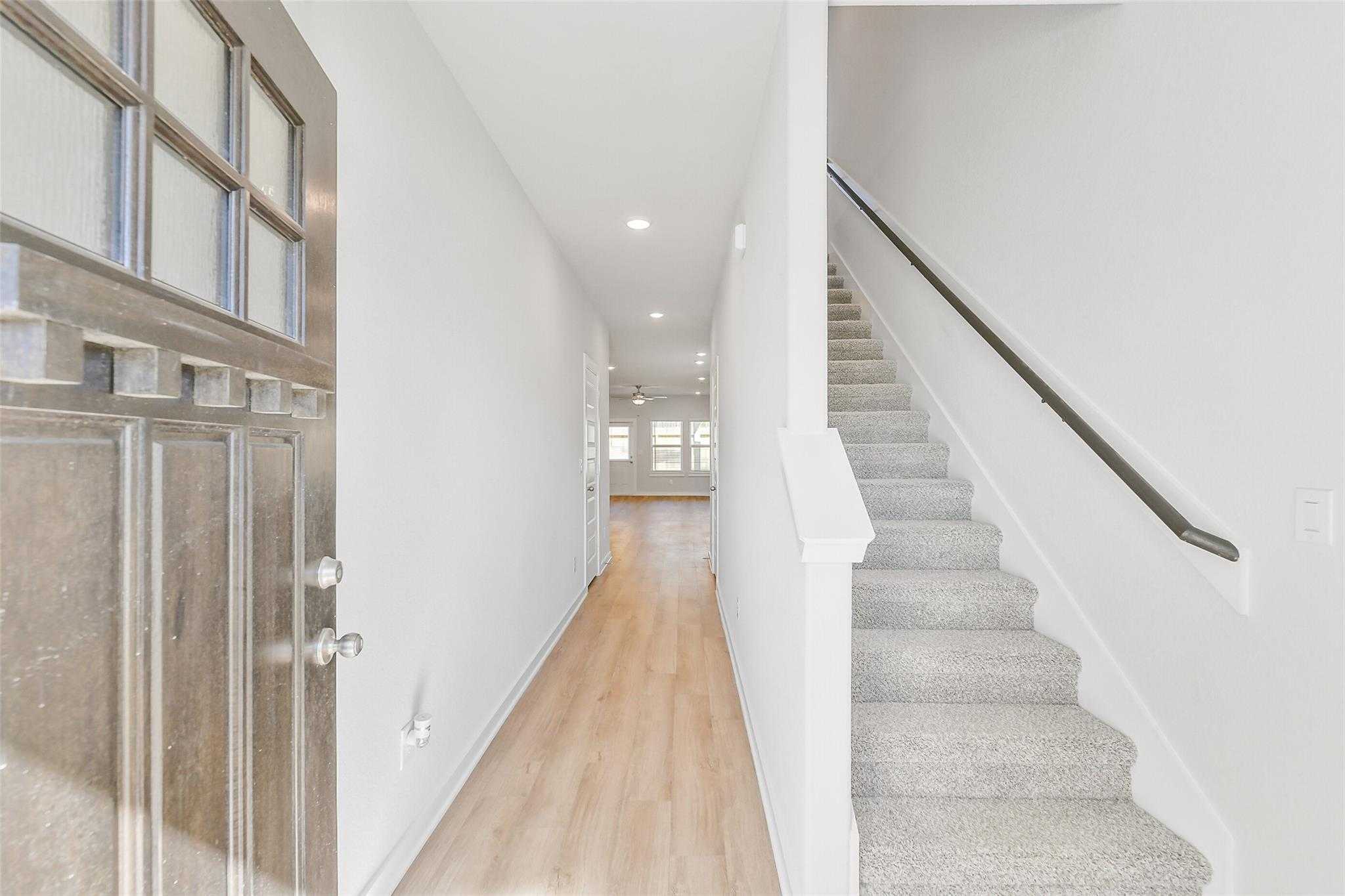 Bright entry foyer with glass-paneled front door, oak hardwood hallway, and carpeted staircase in Davidson Homes The Blanco E, Magnolia, Texas