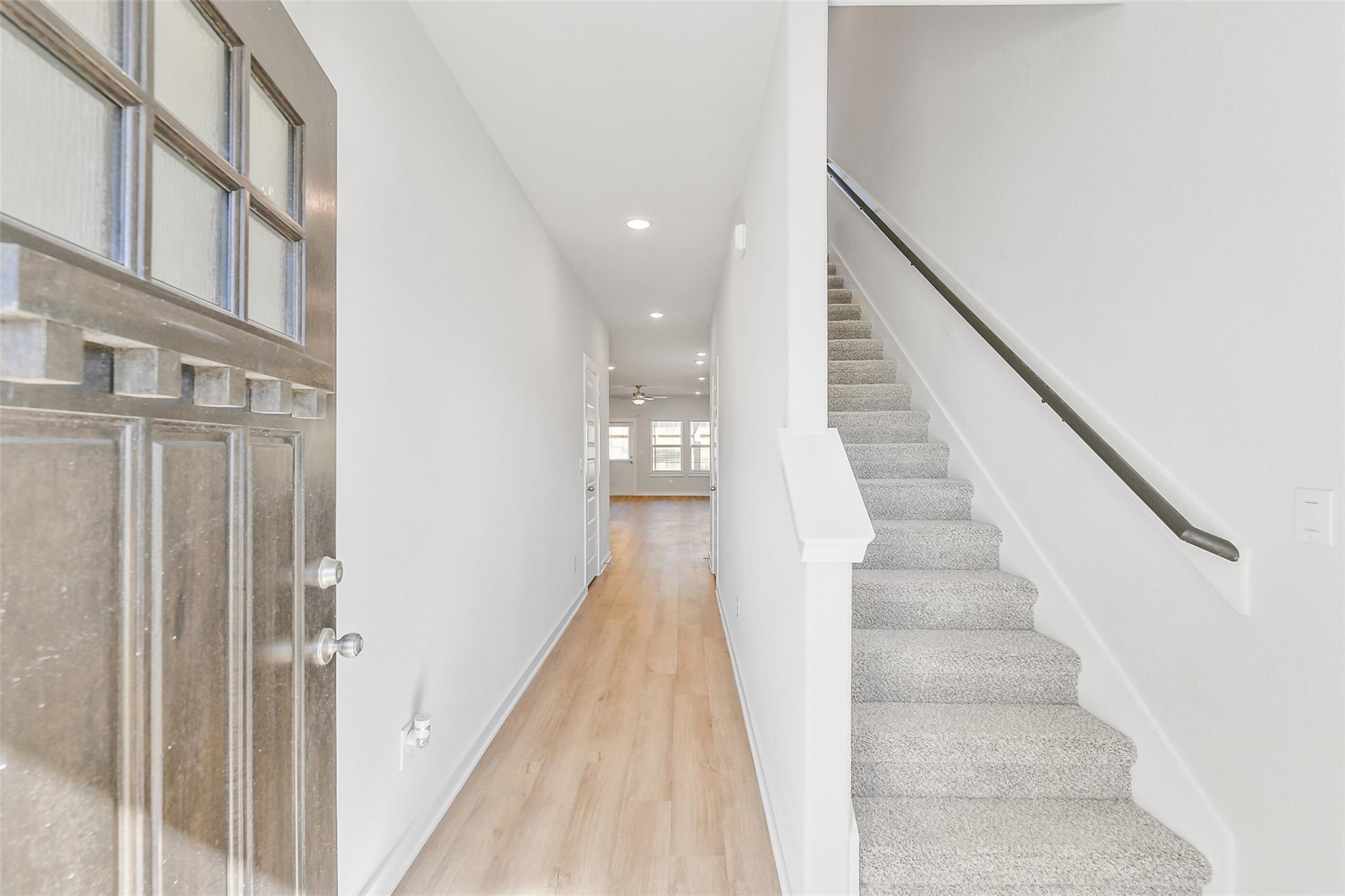 Bright entry foyer with glass-paneled front door, oak hardwood hallway, and carpeted staircase in Davidson Homes The Blanco E, Magnolia, Texas