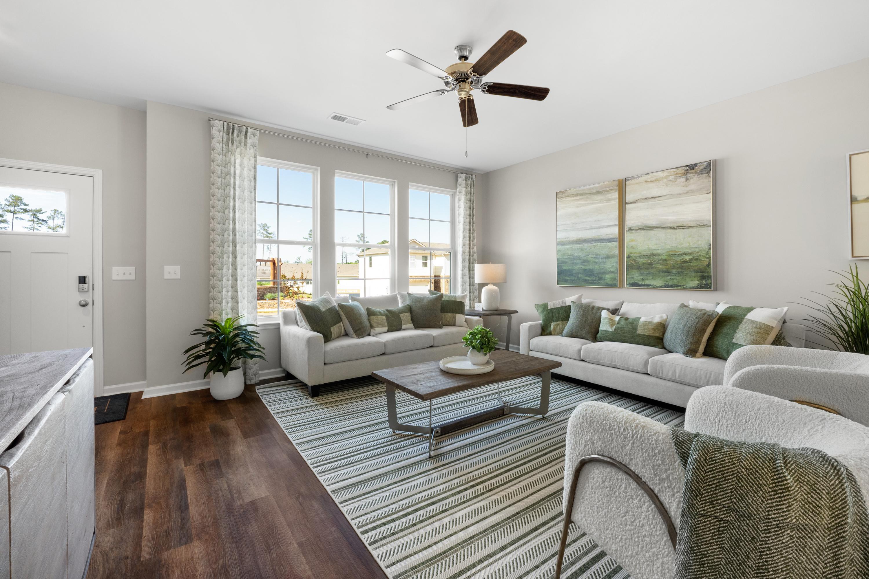 Spacious open-concept living room in Evergreen Mill Madison AL home with beige sofas, ceiling fans, hardwood floors and large windows
