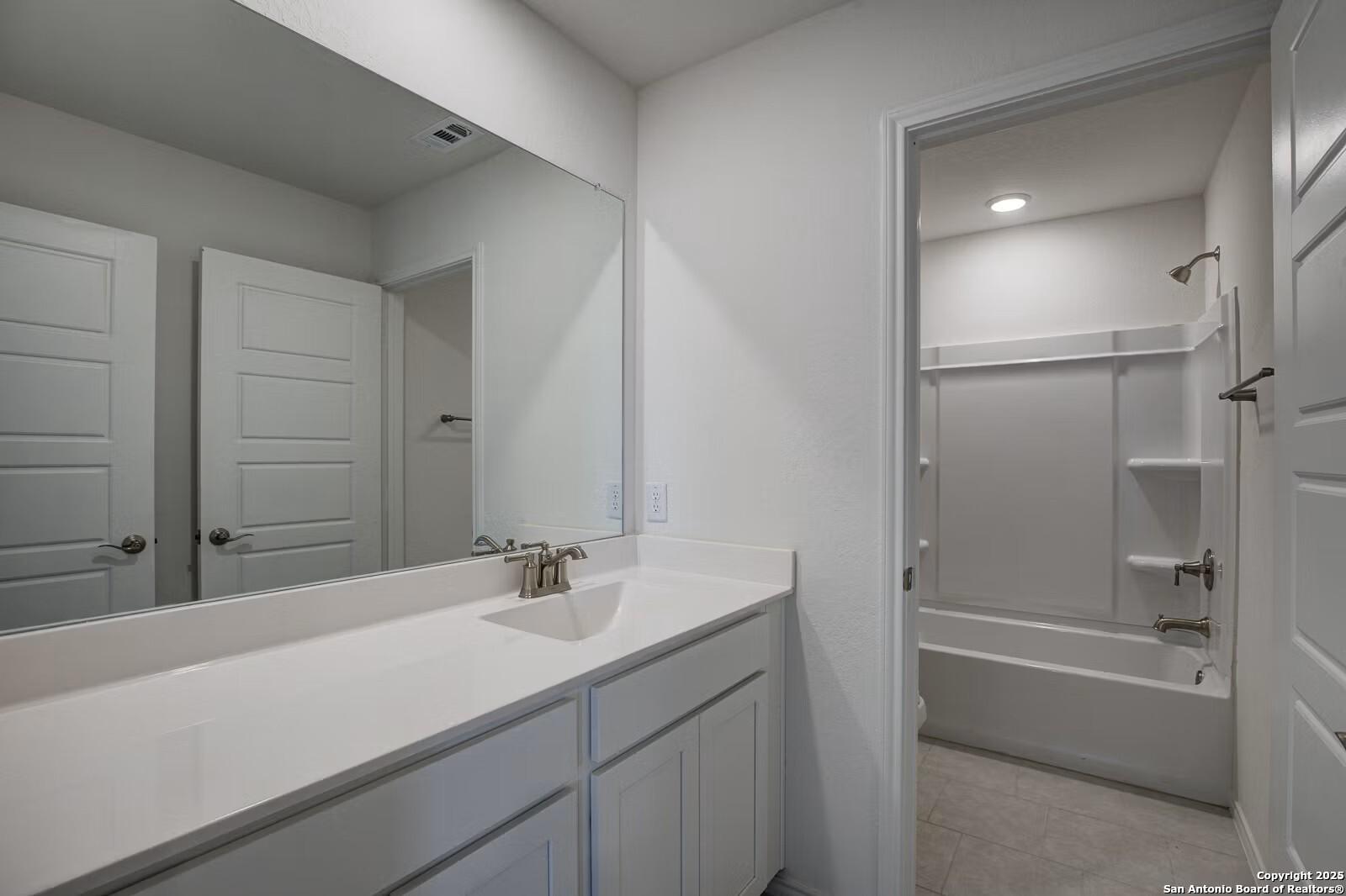 Modern double vanity bathroom with large mirror, tub-shower combo in Davidson Homes The Douglas B, Seguin, Texas