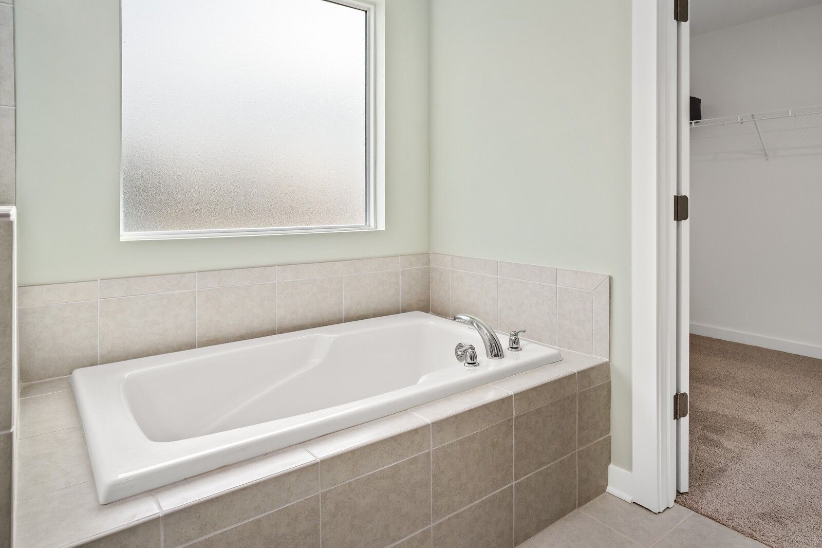 Elegant white bathtub with chrome faucets in tiled master bathroom, frosted window, Davidson Homes Gordon C, Sage Farms White House TN