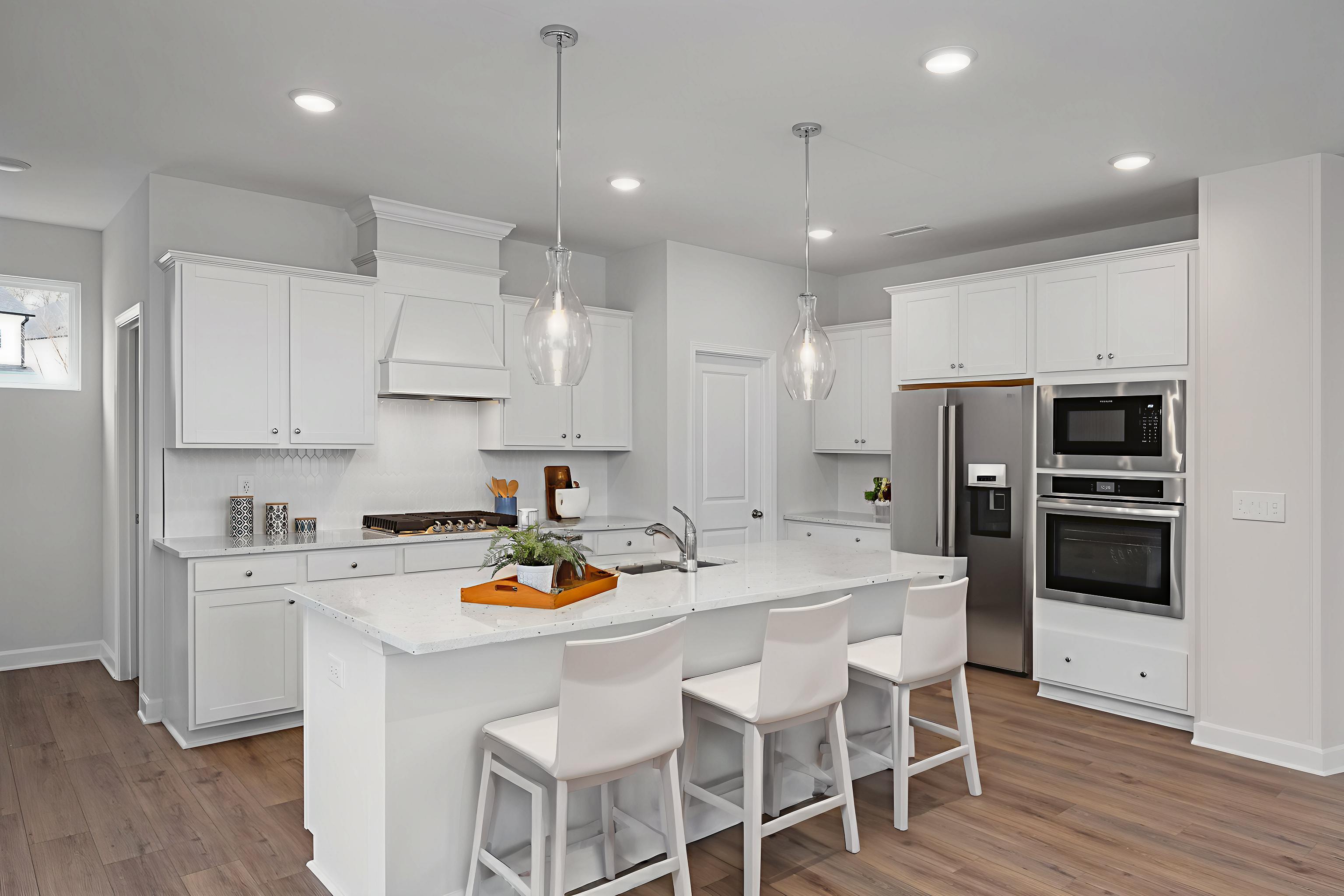 Bright white kitchen with island seating, pendant lights, and stainless appliances at Villas at Carpenter Woods in Durham, NC
