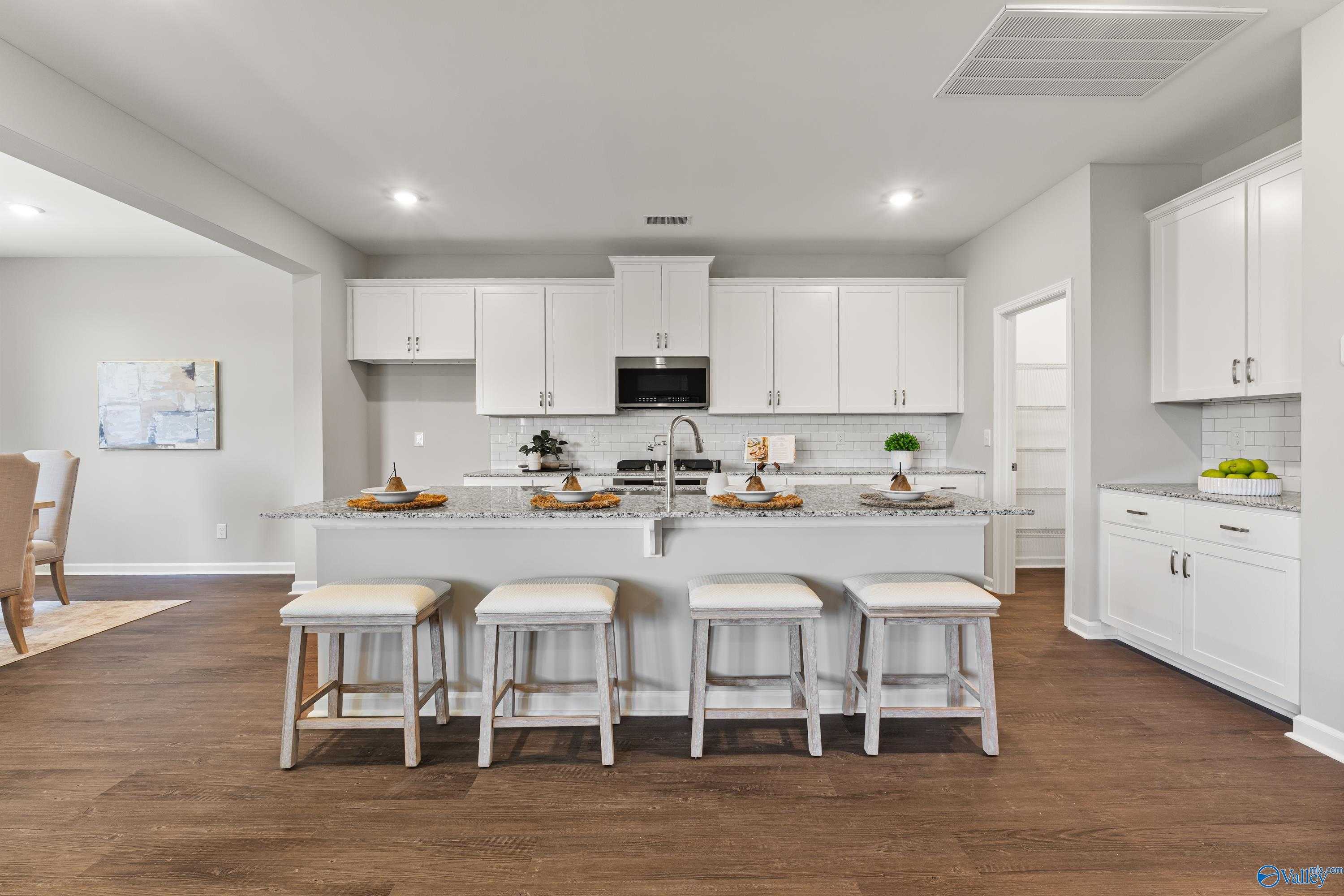 Modern white kitchen island with seating, stainless sink, and hardwood floors in The Avalon floor plan by Davidson Homes, Huntsville AL