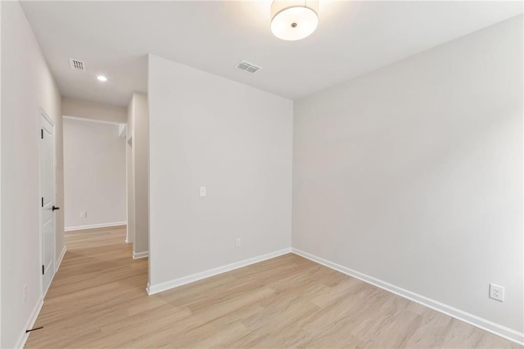 Bright secondary bedroom with light oak hardwood floors and neutral white walls in Davidson Homes The Daphne C, Loganville, GA