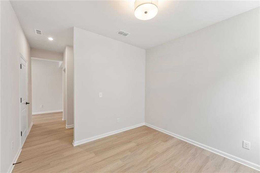 Bright bedroom with light oak floors, neutral walls, hallway access, and ceiling fixture in The Daphne C by Davidson Homes, Loganville, GA