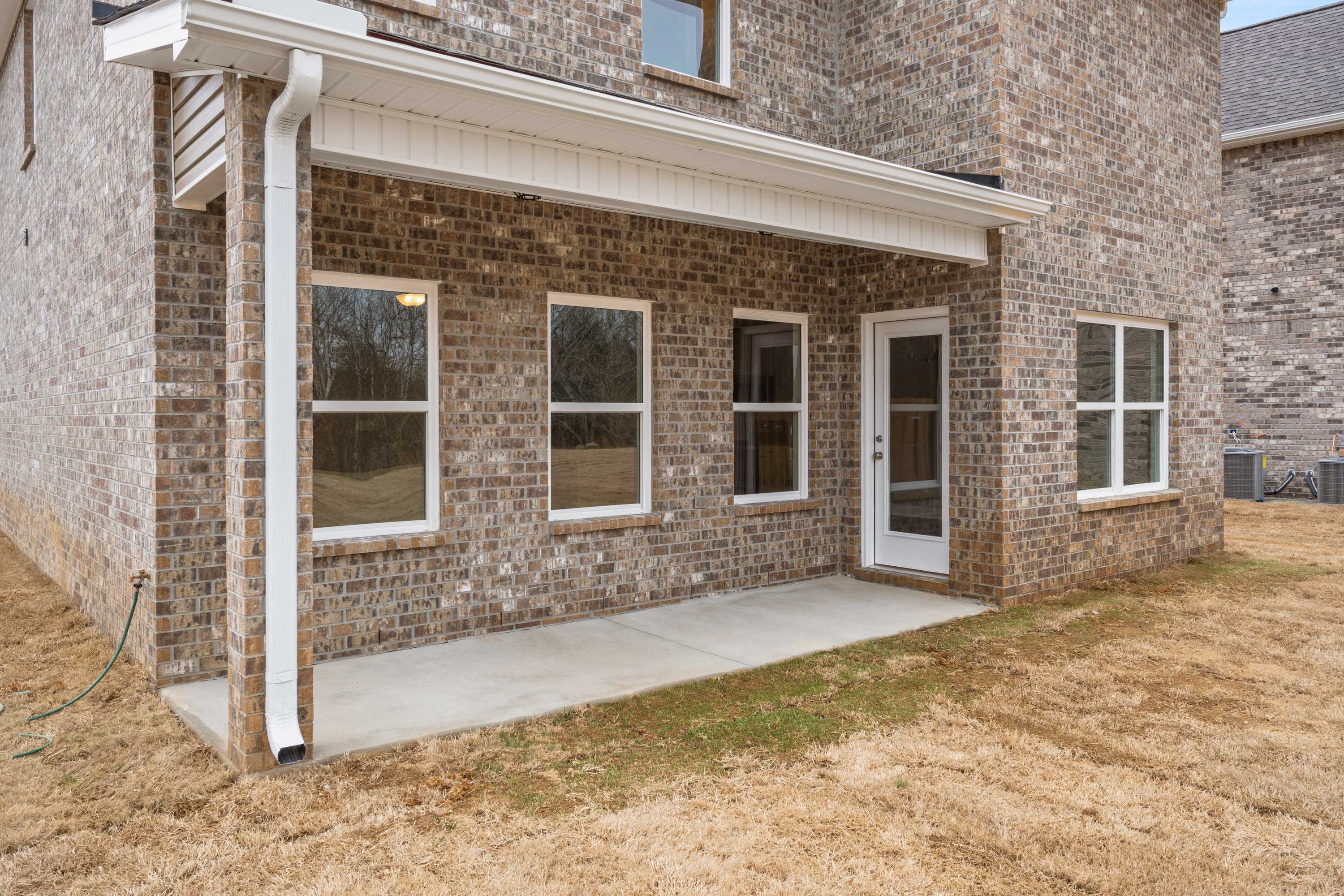 Rear elevation of The Aiken two-story home showcasing brick exterior, covered porch, and glass door to backyard in Meridianville