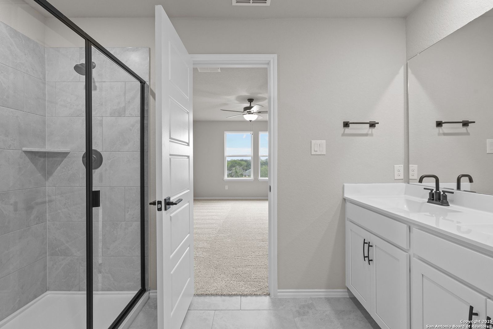Modern master bathroom with frameless glass shower, double vanity, and bedroom view in Davidson Homes The Murray J, San Antonio