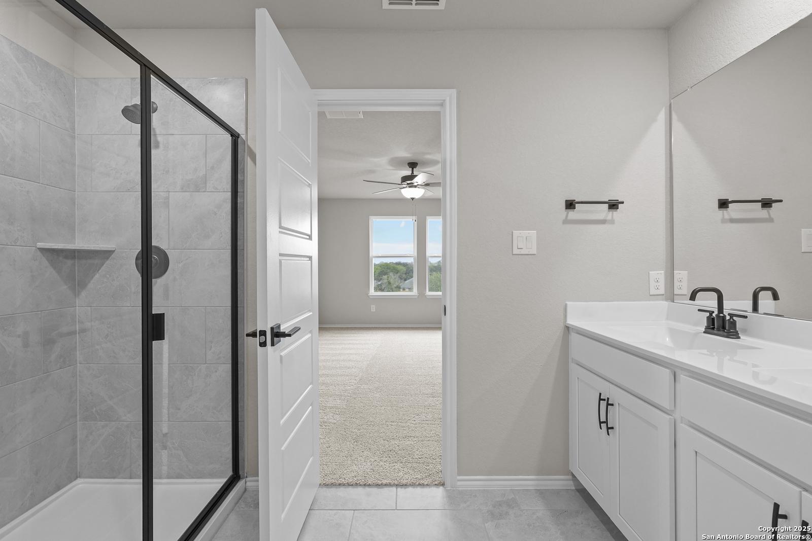 Modern master bathroom with frameless glass shower, double vanity, and bedroom view in Davidson Homes The Murray J, San Antonio