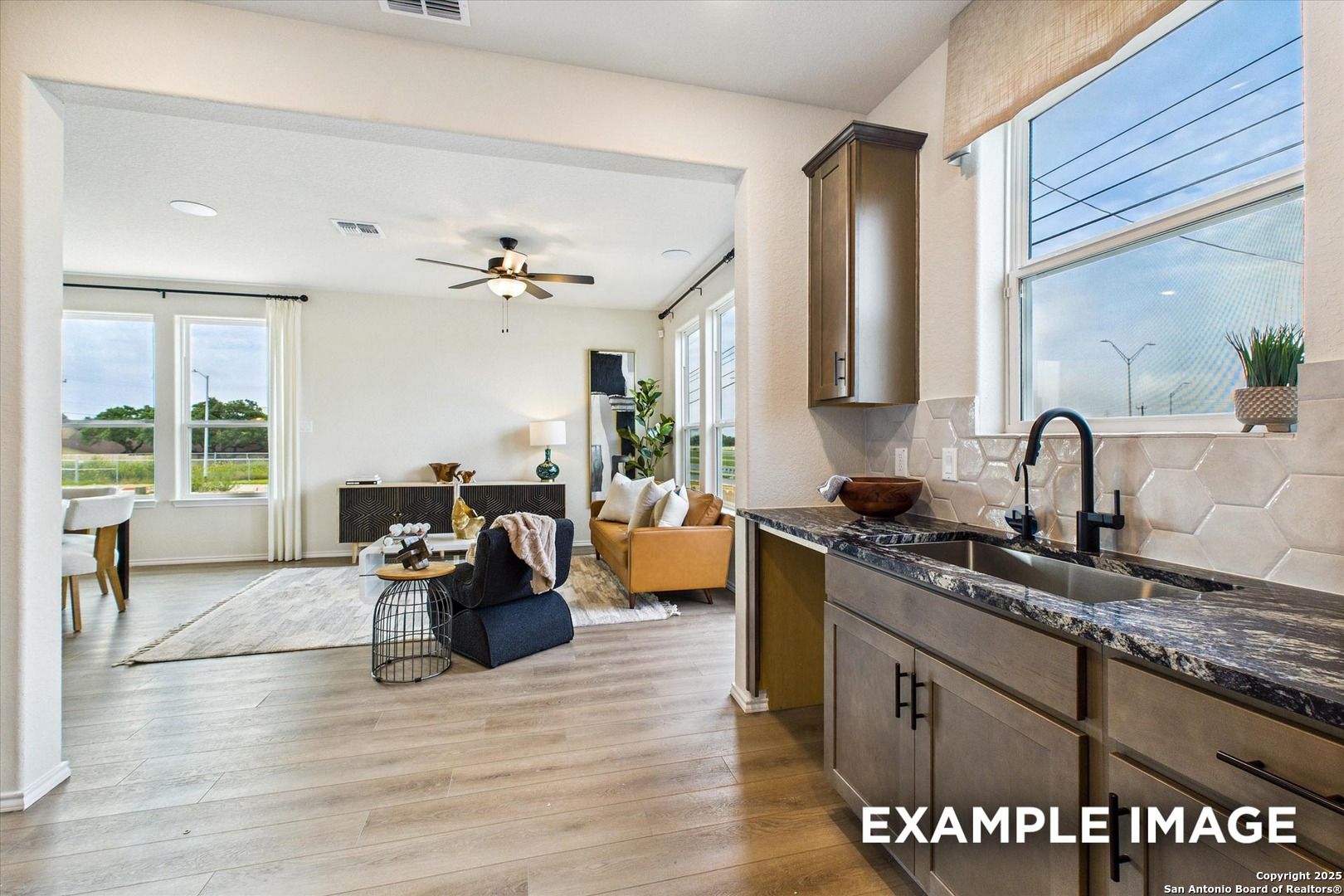 Open-concept living room and kitchen with wood cabinets, black faucet, granite counters, and large windows in Davidson Homes The Florence C, San Antonio