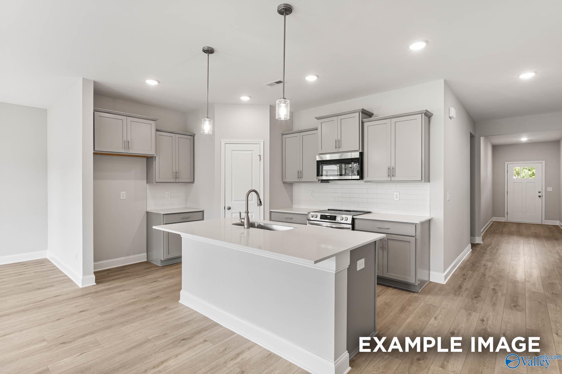 Modern open-concept kitchen with gray shaker cabinets, stainless appliances, large island sink, and hardwood floors in Davidson Homes The Daphne, Hazel Green, AL