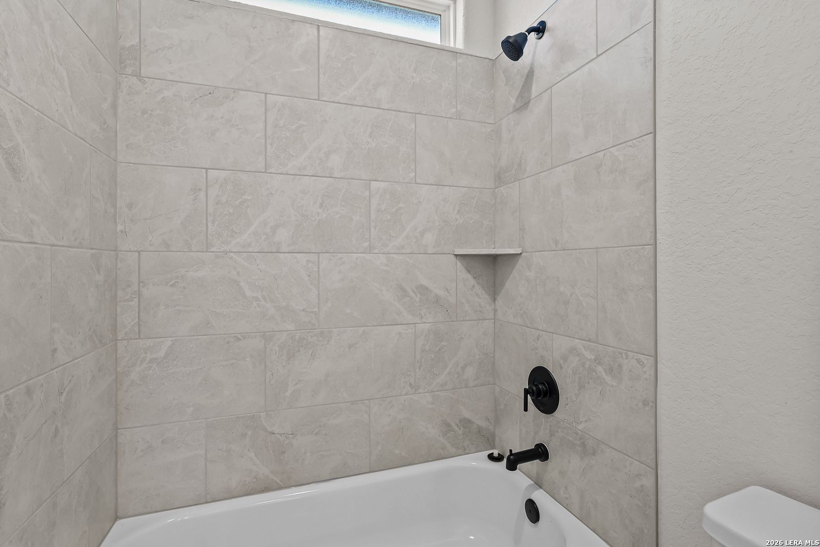 Modern bathroom with tile surround bathtub, matte black fixtures, and corner shelf in Davidson Homes' Oxford F plan, Castroville, TX