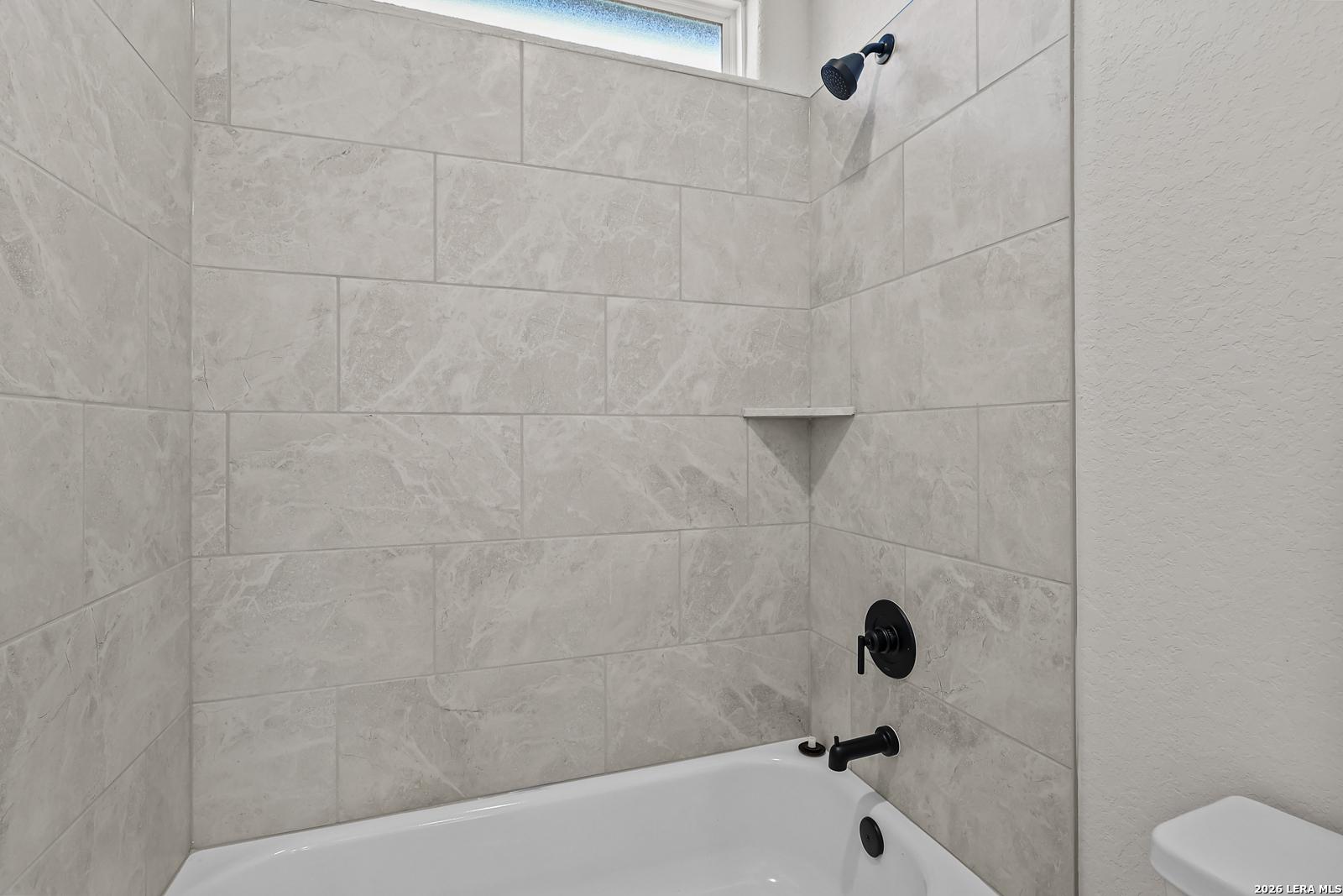 Modern bathroom with tile surround bathtub, matte black fixtures, and corner shelf in Davidson Homes' Oxford F plan, Castroville, TX