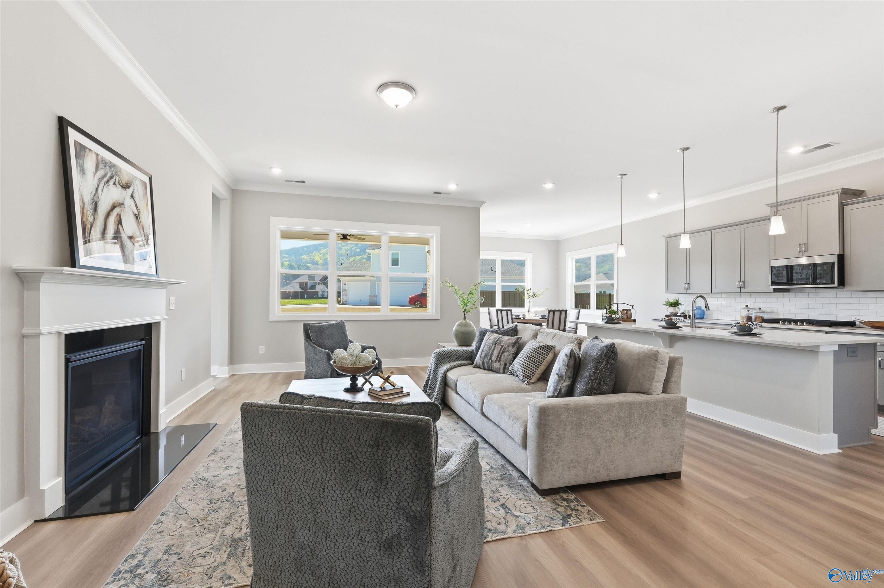 Open-concept living room with gas fireplace, gray sectional sofa, and modern kitchen island in Evermore Homes The Oxford B, Owens Cross Roads, Alabama
