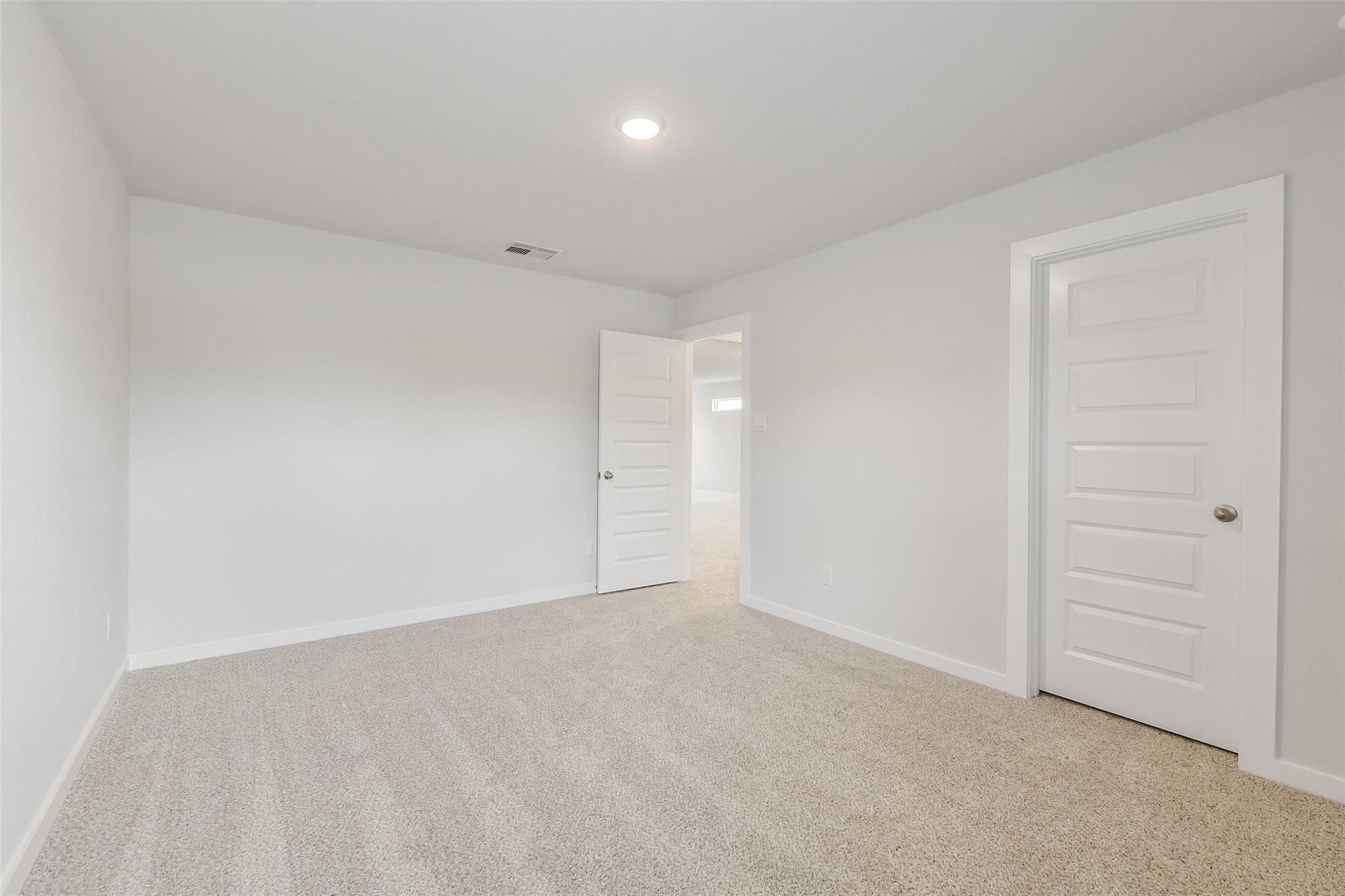 Empty bedroom with beige carpet, white walls, recessed lighting, and open door to hallway in Davidson Homes San Marcos E, Conroe Texas