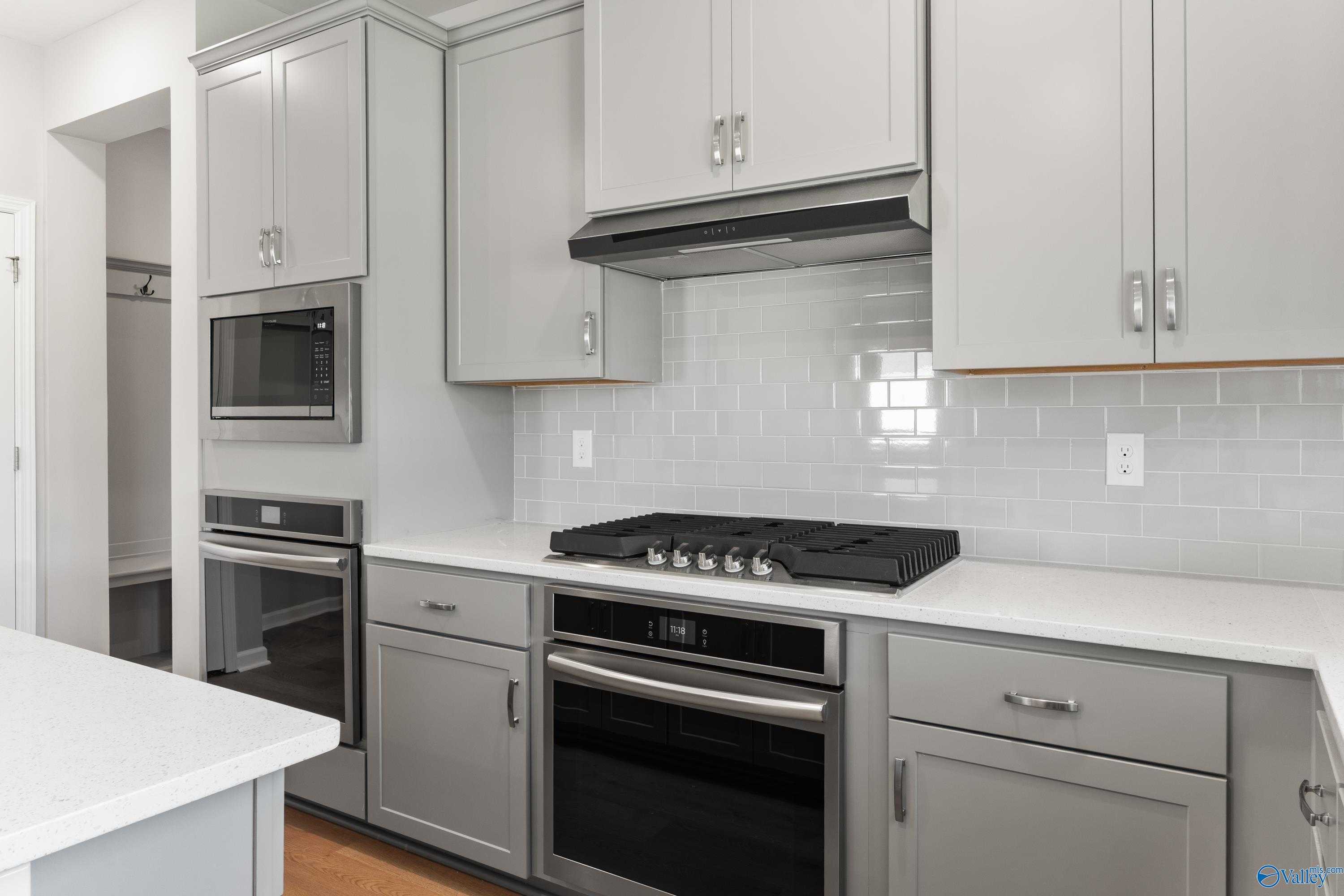 Modern kitchen featuring gray shaker cabinets, stainless steel gas range, and white subway tile backsplash in Davidson Homes The Charm, Huntsville, AL