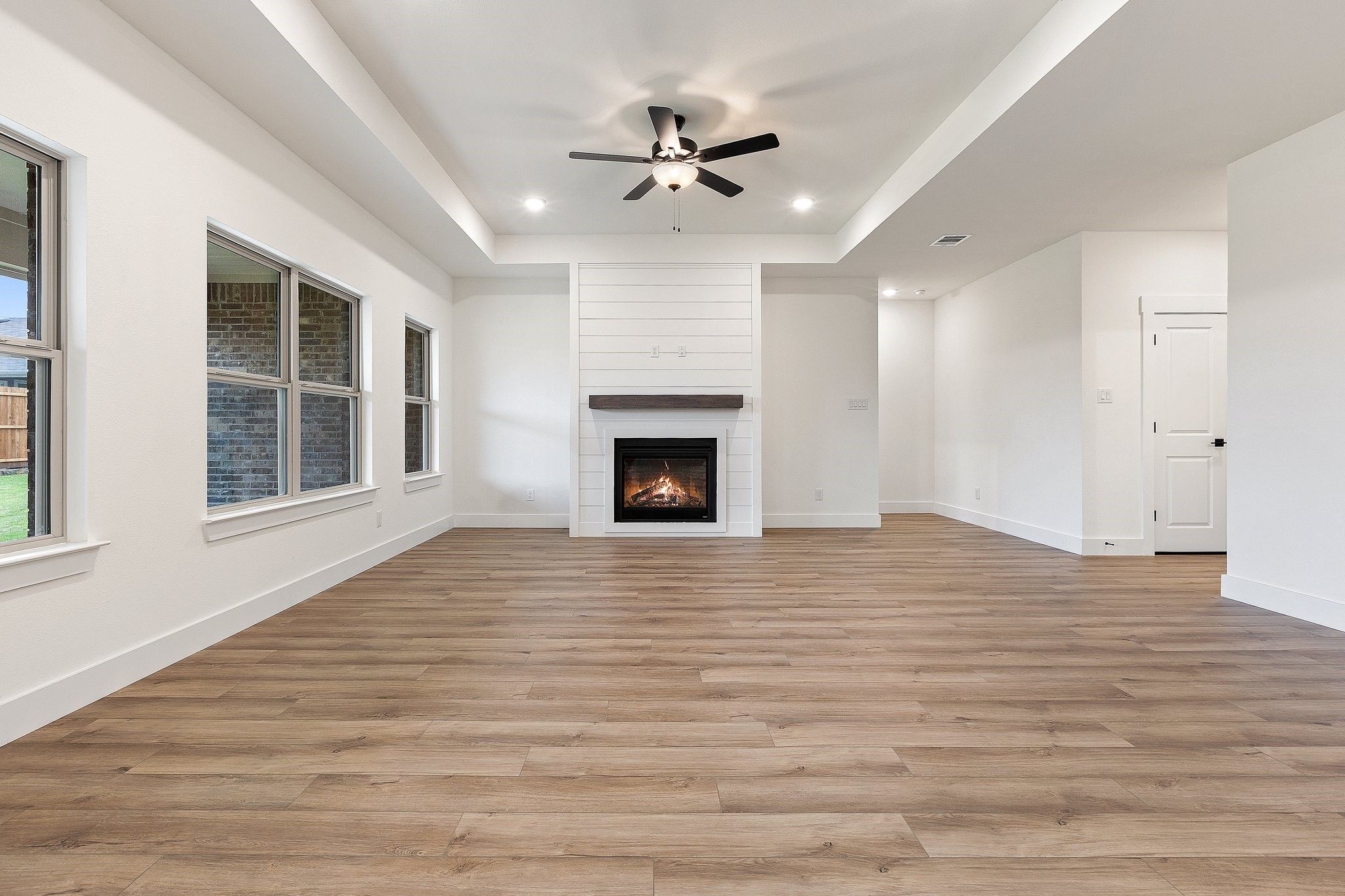 Spacious living room with tray ceiling, fireplace, and wood-style flooring in The Rockford C plan at Waverly Estates.