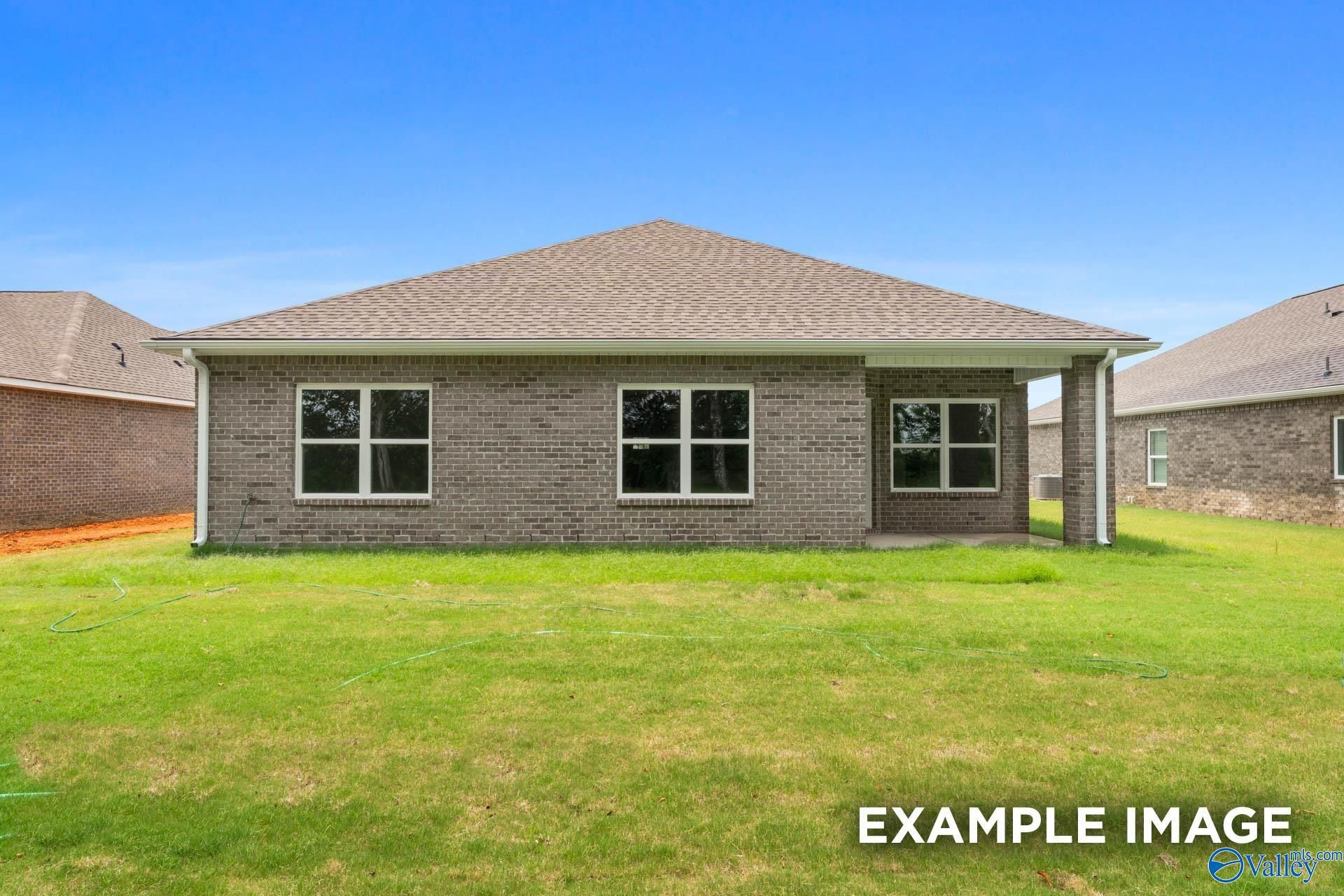 Rear view of single-story brick Daphne E home with covered patio, large windows, and lush green backyard in Harvest, Alabama