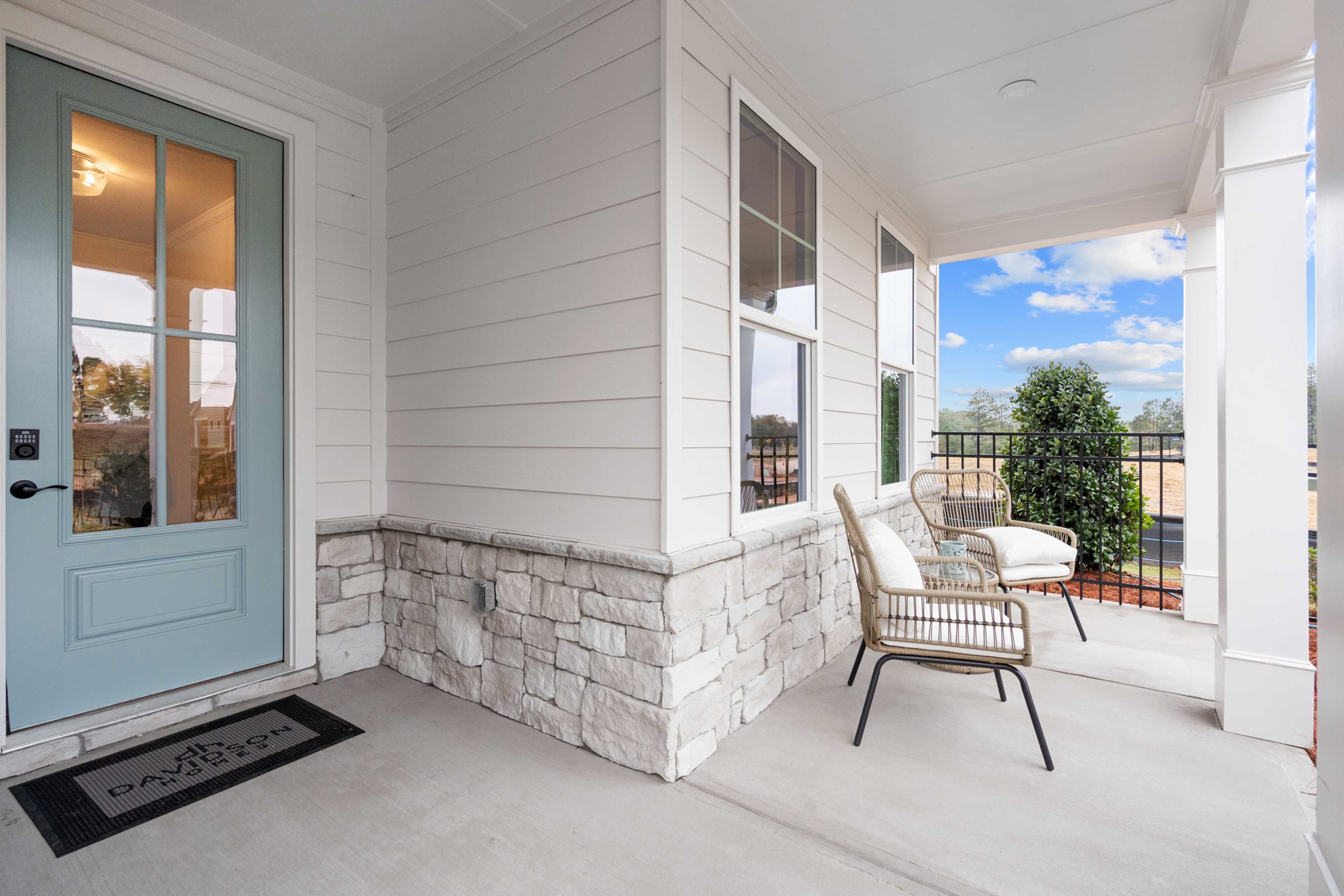 Covered front porch at Kelly Preserve in Loganville GA with wicker chairs, blue glass door, and stone accents