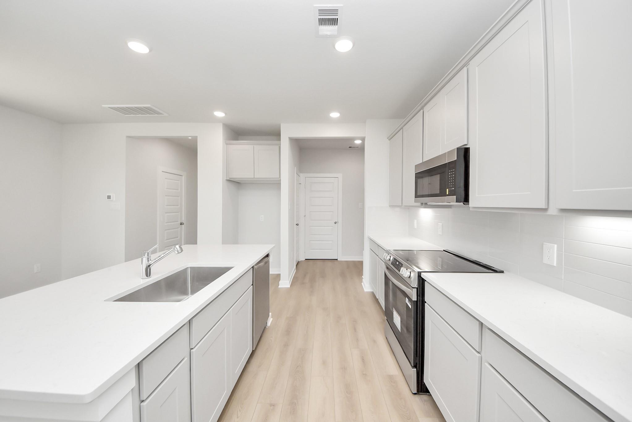 Modern kitchen with white cabinets, quartz countertops, and stainless appliances in The Blanco F, Spring Branch Crossing.