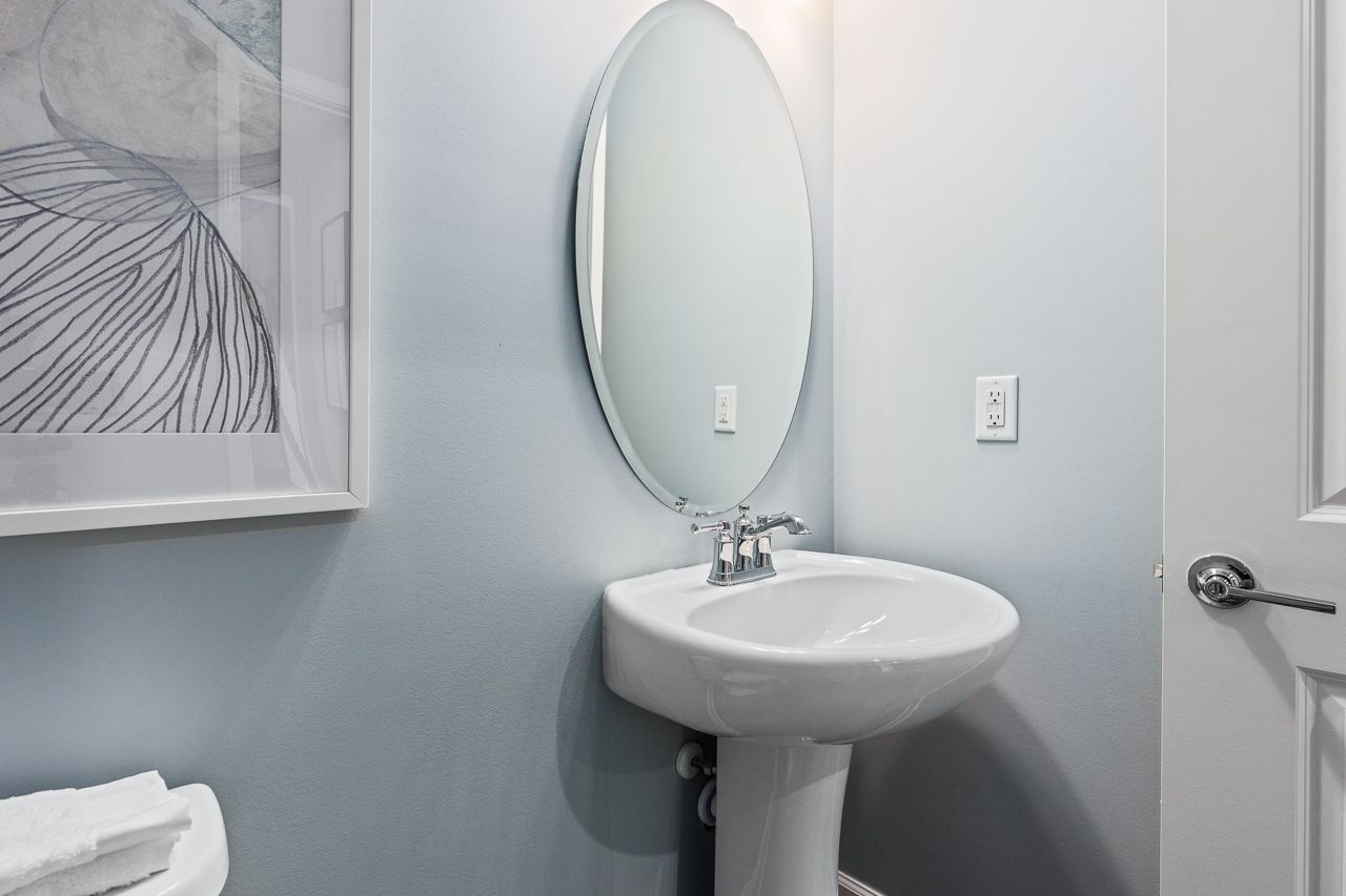 Modern powder room in The Hemlock floor plan featuring a sleek pedestal sink, oval mirror, and blue-toned walls.
