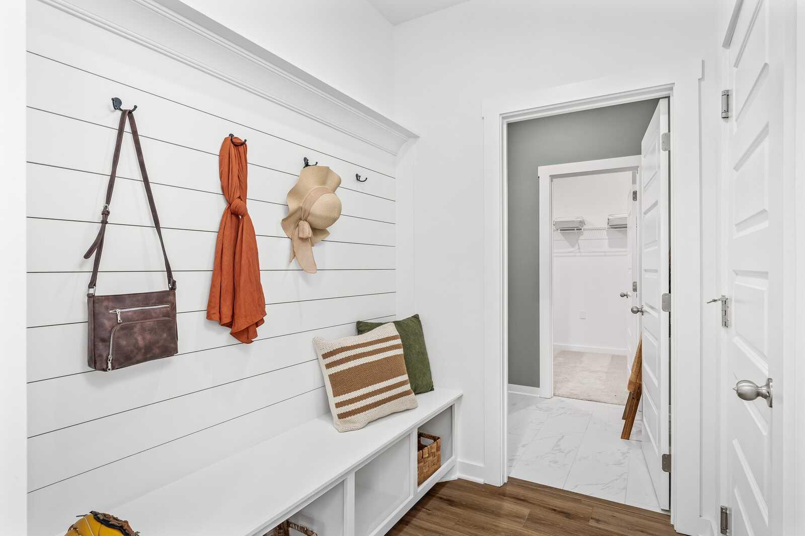 White shiplap mudroom at Calista Farms in White House TN with built-in bench, hanging purses, scarf, hat, and open bathroom door