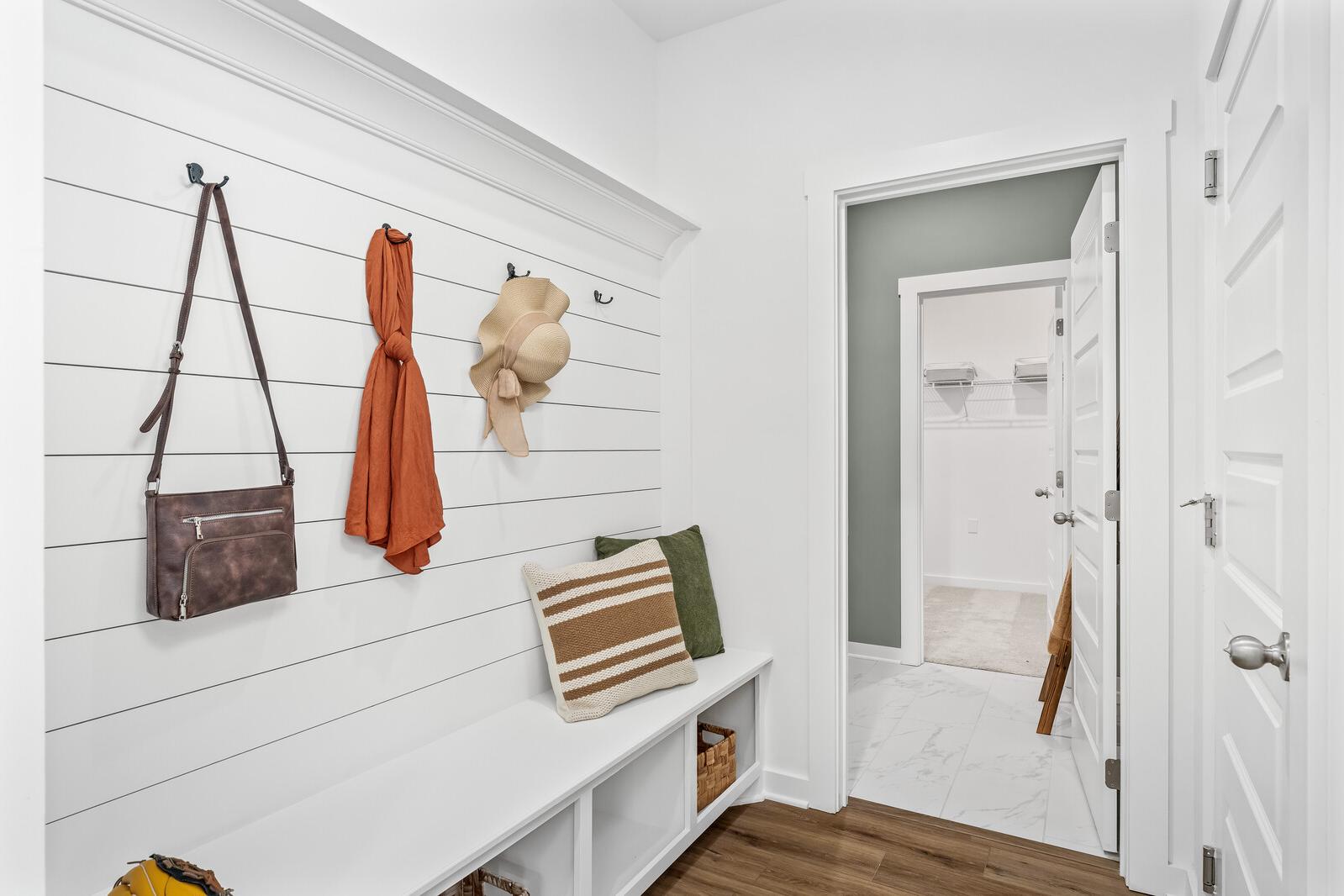 White shiplap mudroom at Calista Farms in White House TN with built-in bench, hanging purses, scarf, hat, and open bathroom door